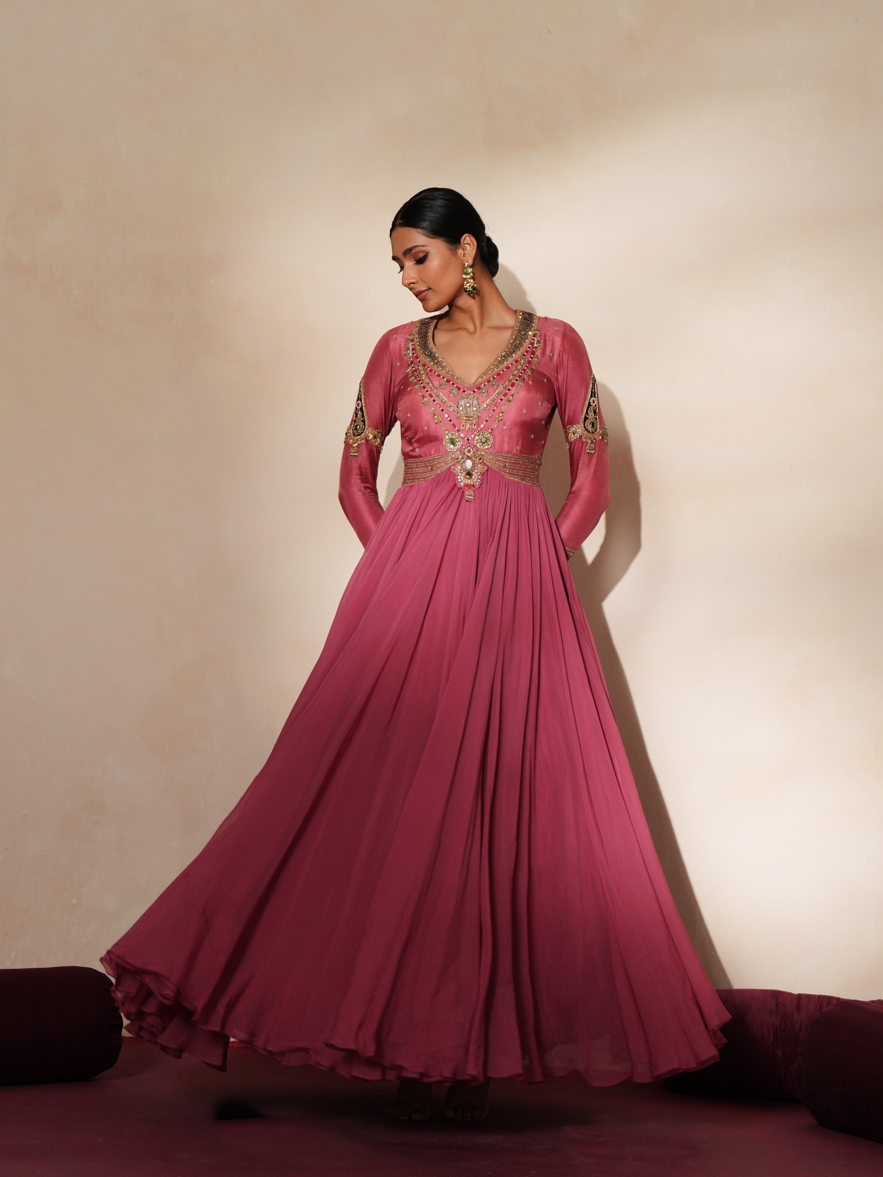 Woman in a mauve pink traditional outfit standing againsta beige wall on a red carpet.