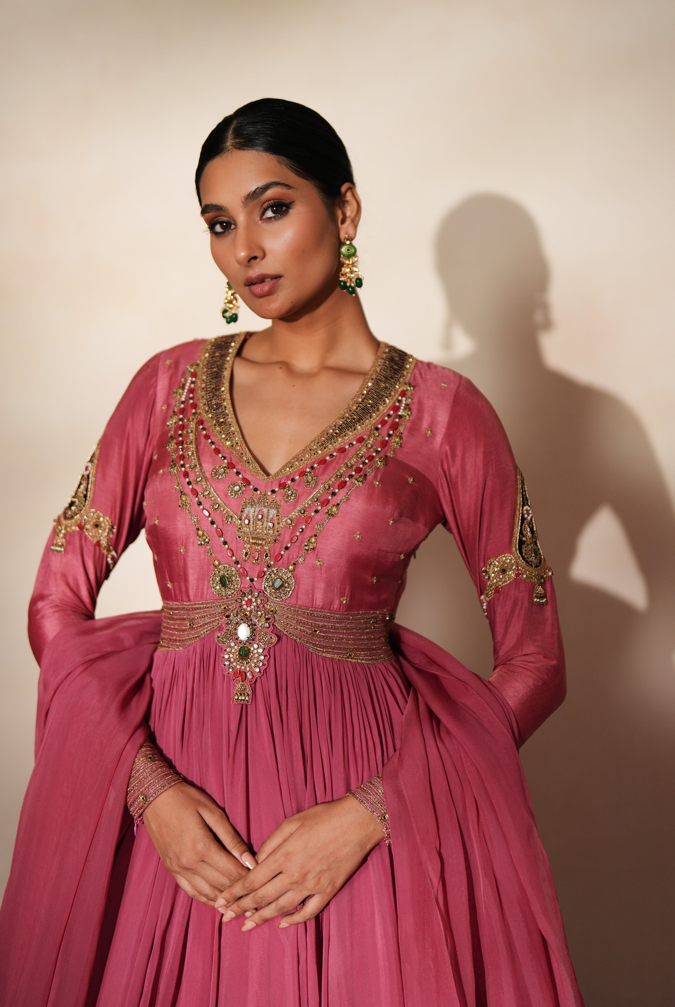 Woman in a mauve pink traditional outfit standing againsta beige wall on a red carpet.