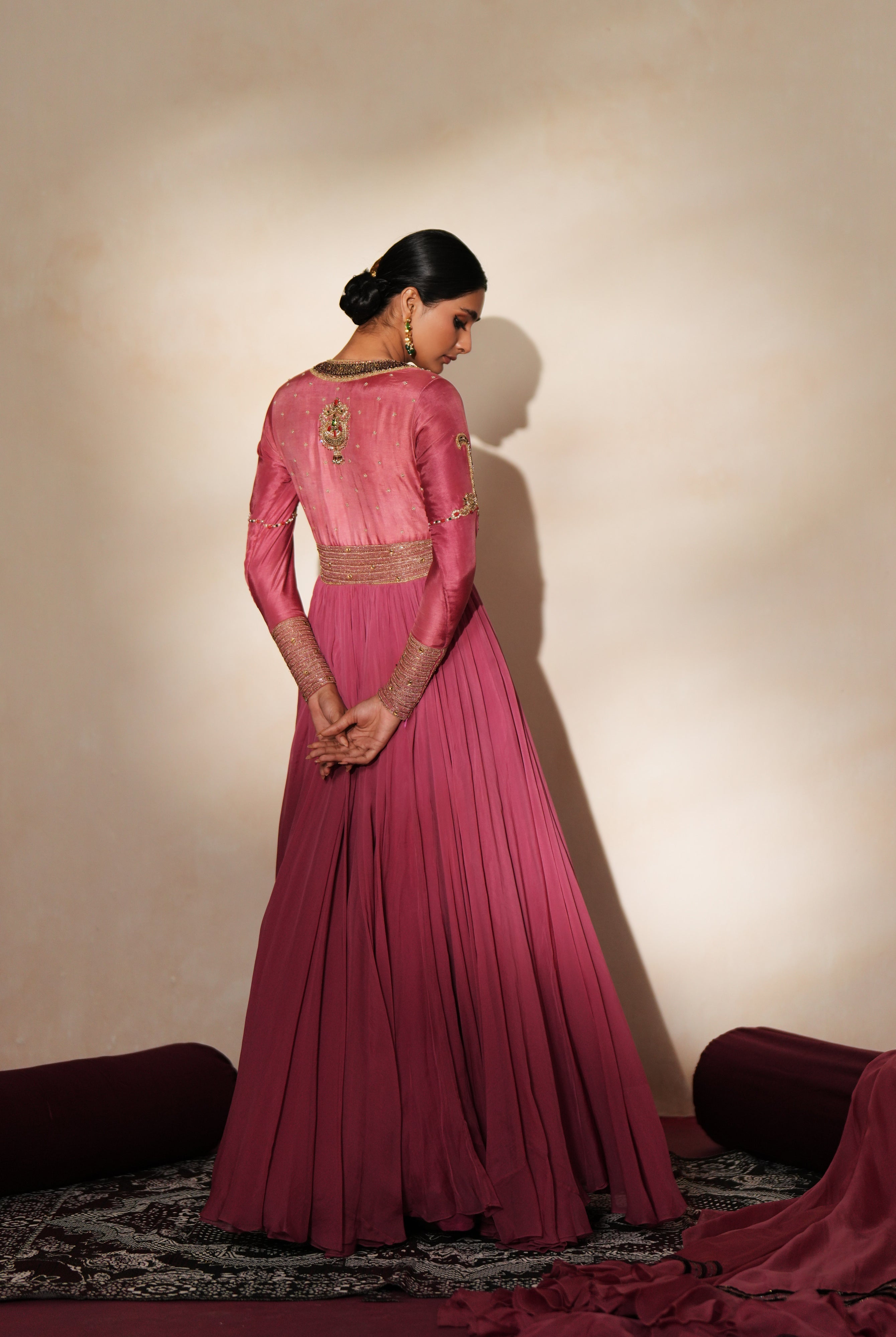 Woman in a mauve pink traditional outfit standing againsta beige wall on a red carpet.