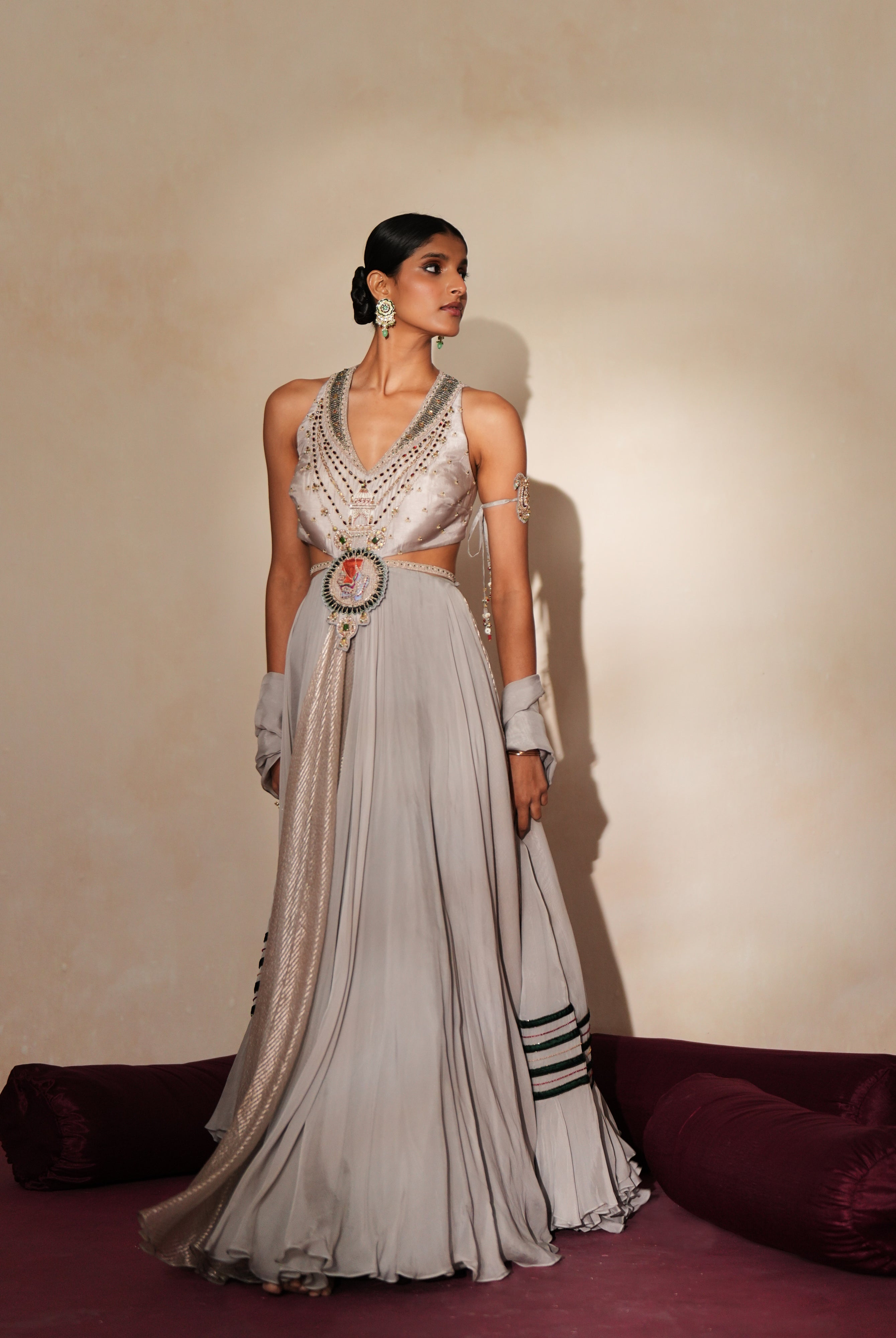 Woman in a mettalic grey traditional outfit standing againsta beige wall on a red carpet.