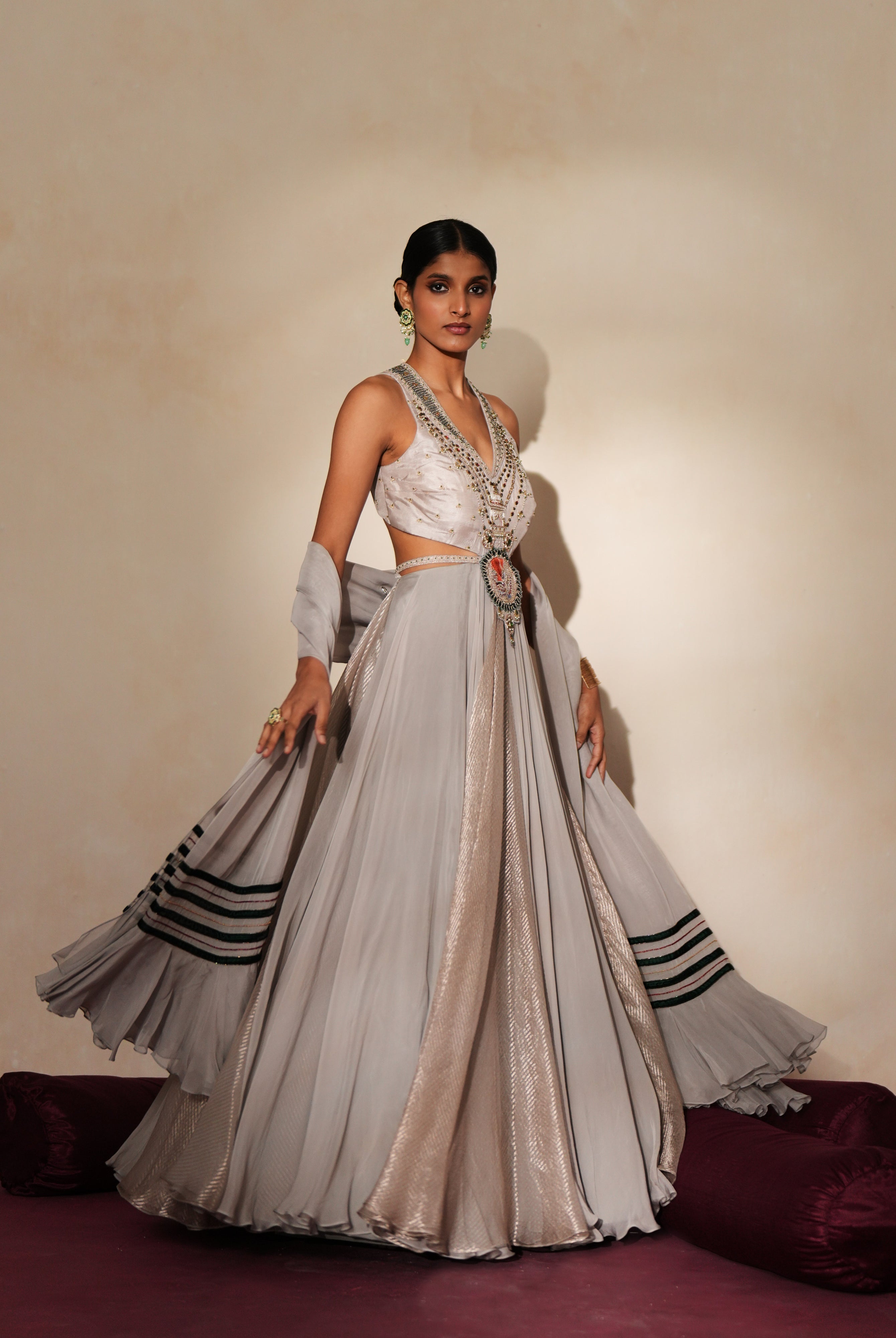 Woman in a mettalic grey traditional outfit standing againsta beige wall on a red carpet.