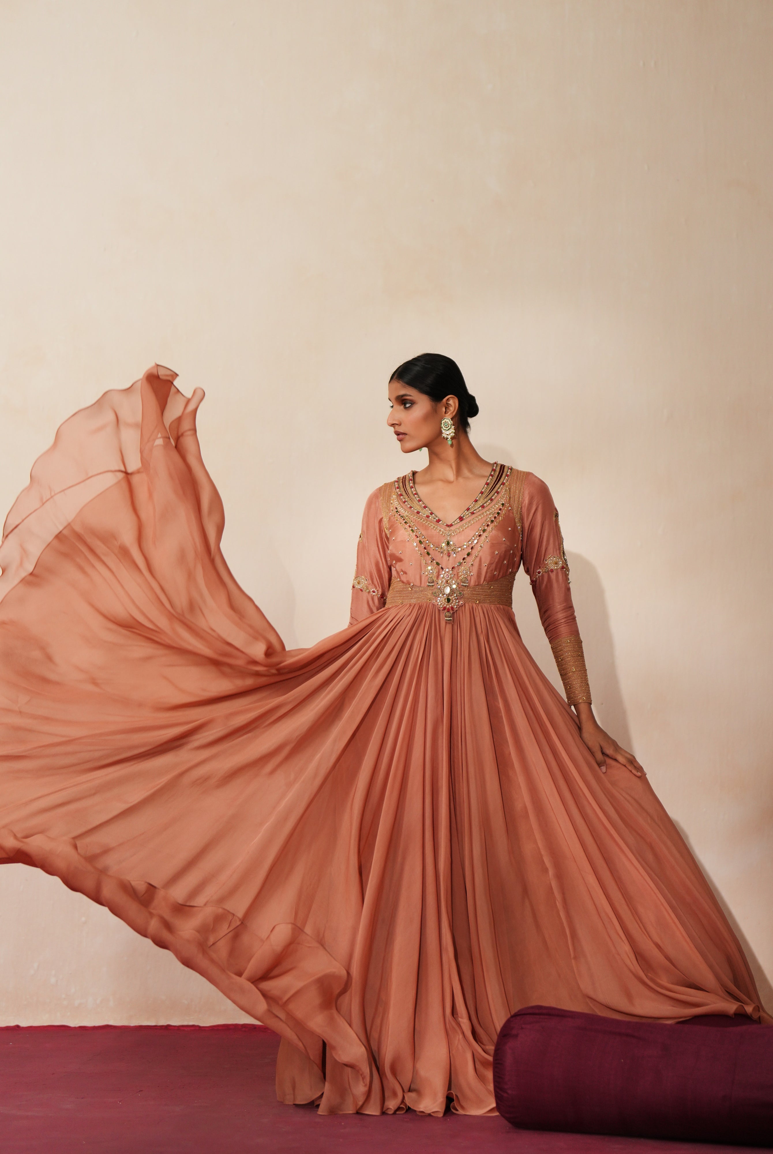 Woman in a metallic mocha traditional outfit standing againsta beige wall on a red carpet.