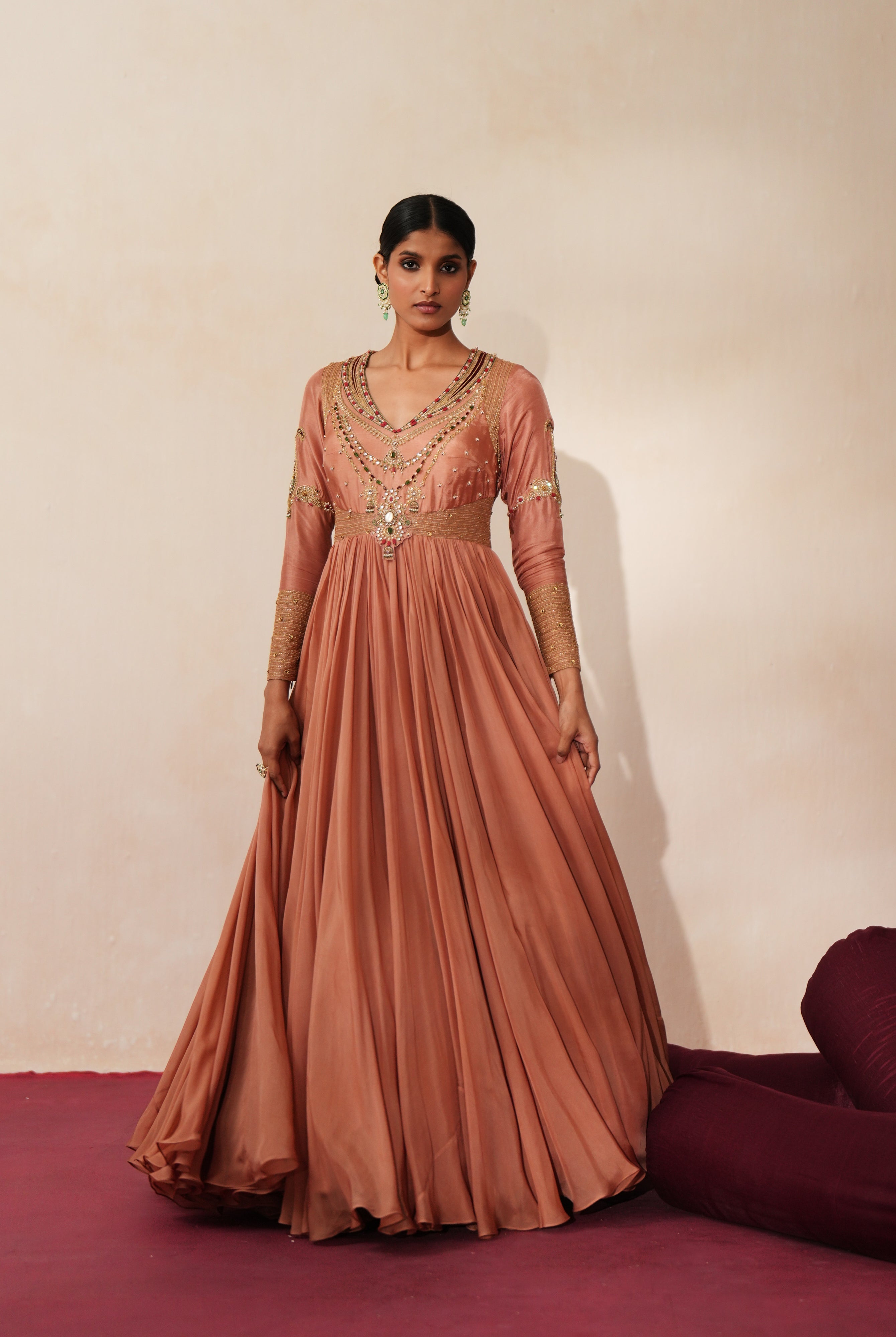 Woman in a metallic mocha traditional outfit standing againsta beige wall on a red carpet.