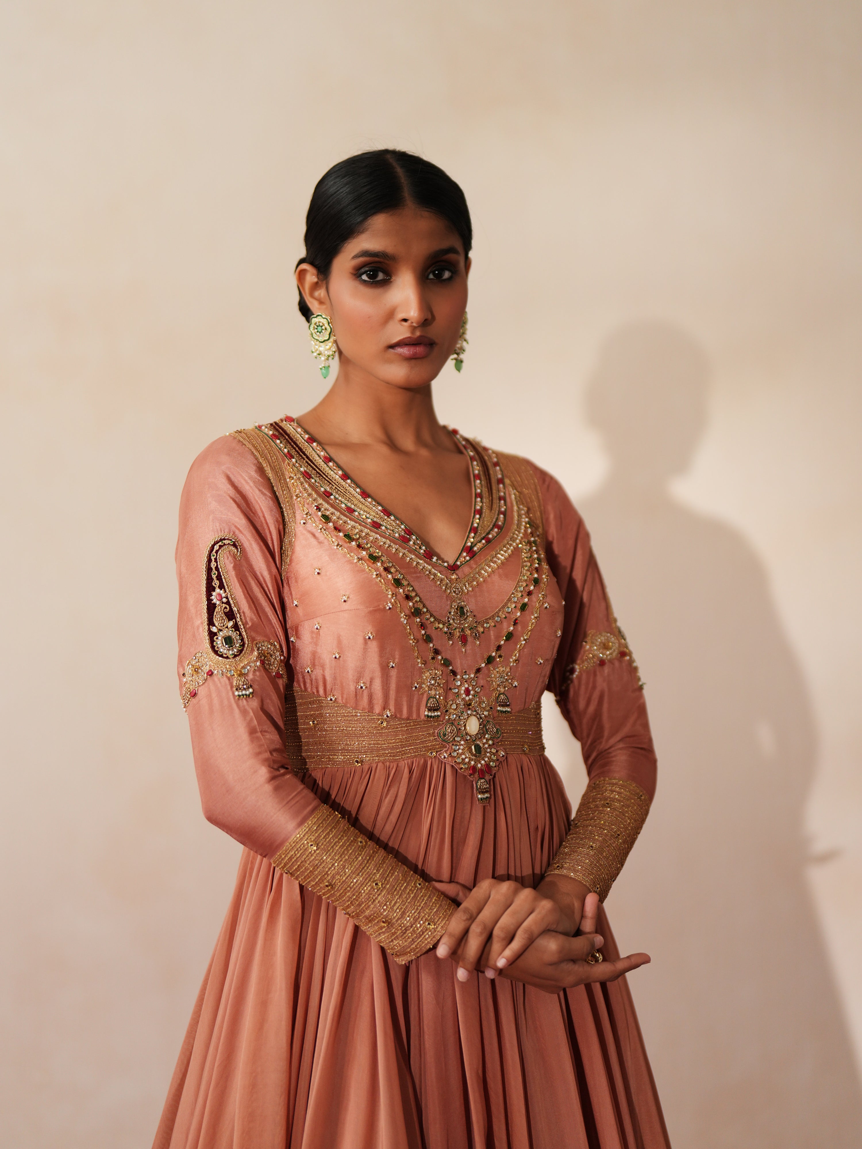 Woman in a metallic mocha traditional outfit standing againsta beige wall on a red carpet.