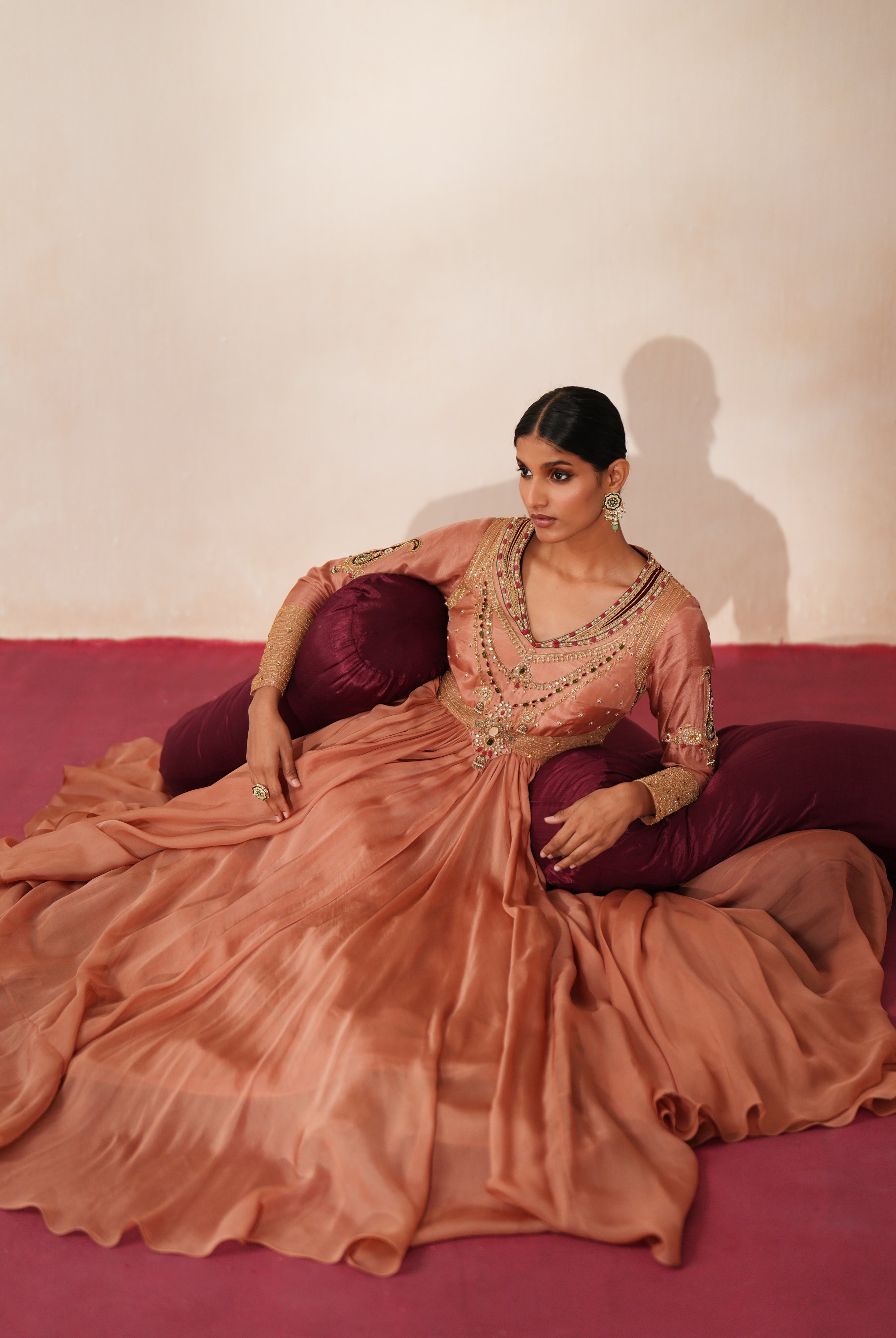Woman in a metallic mocha traditional outfit standing againsta beige wall on a red carpet.