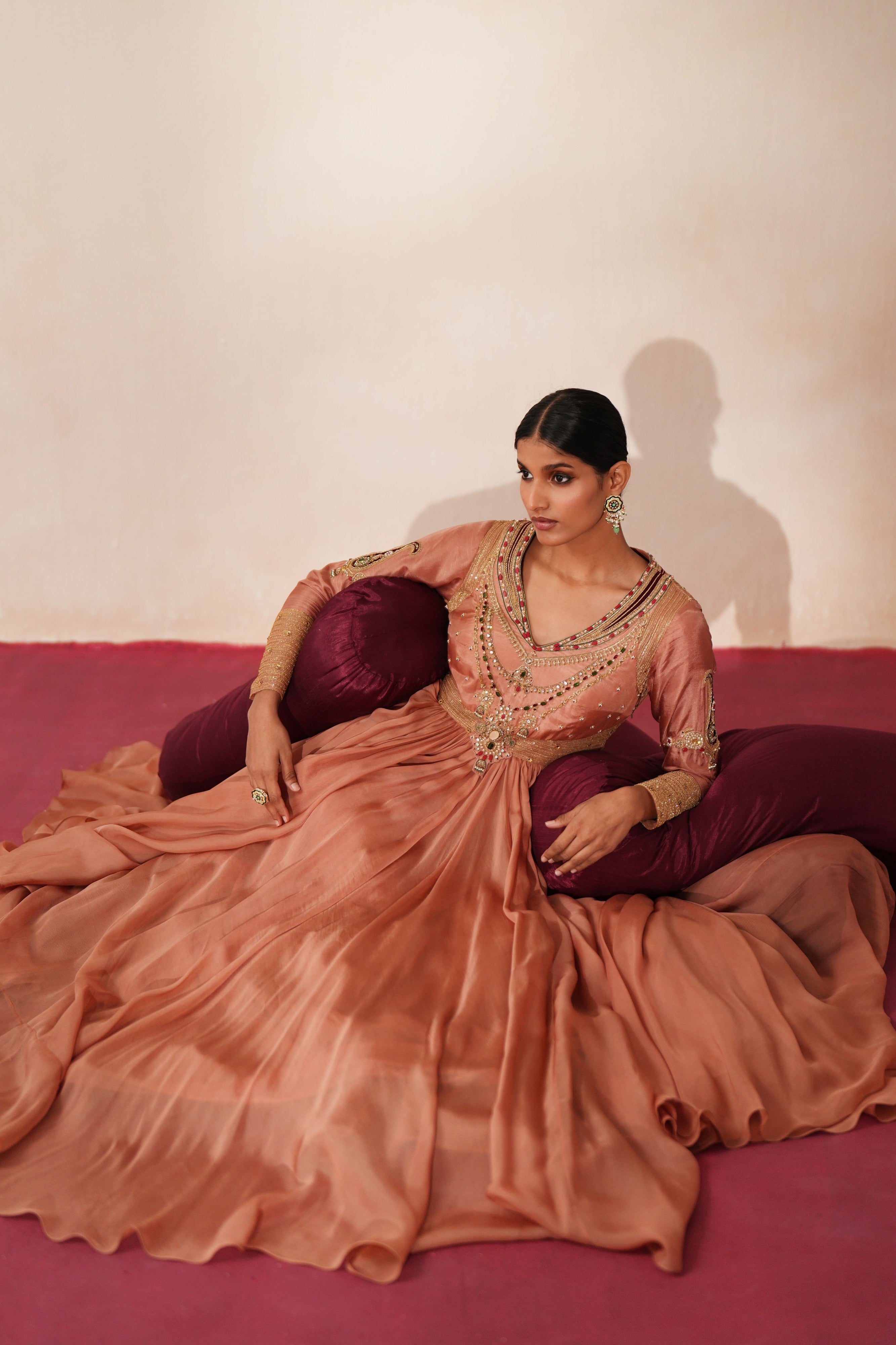 Woman in a metallic mocha traditional outfit standing againsta beige wall on a red carpet.