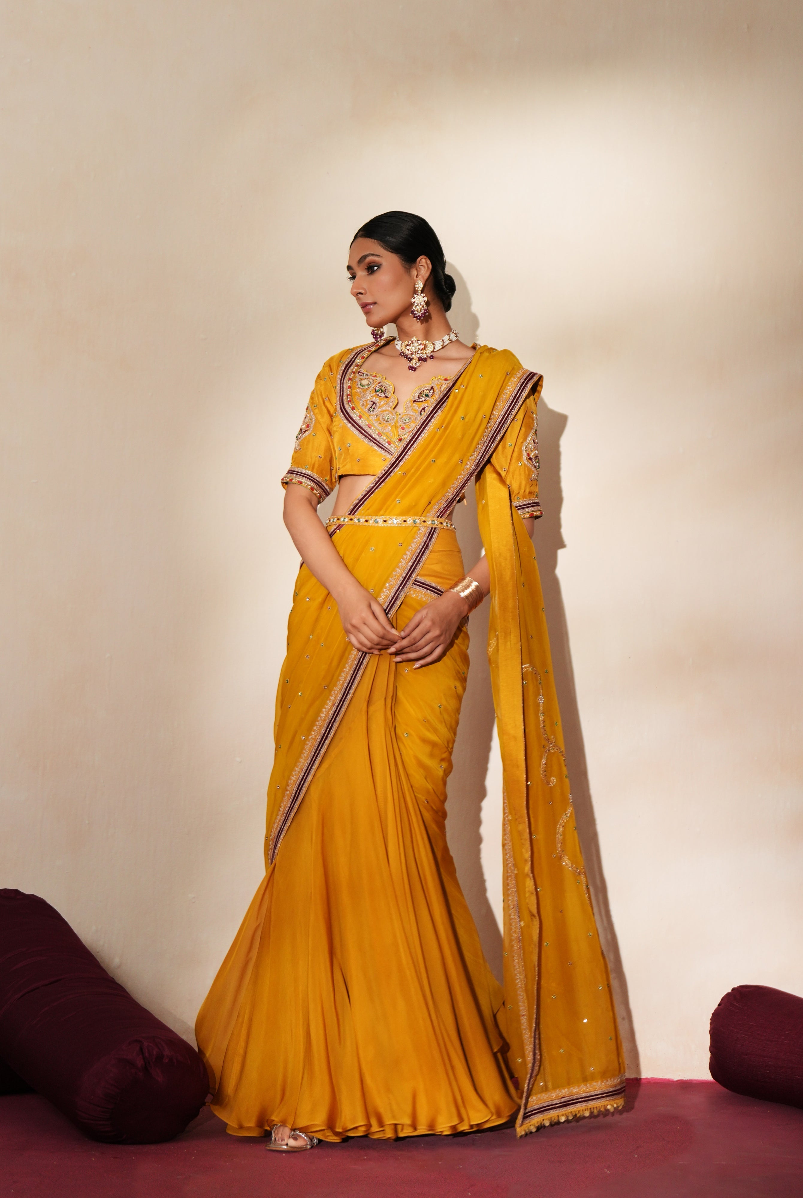 Woman in a golden yellow traditional outfit standing againsta beige wall on a red carpet.