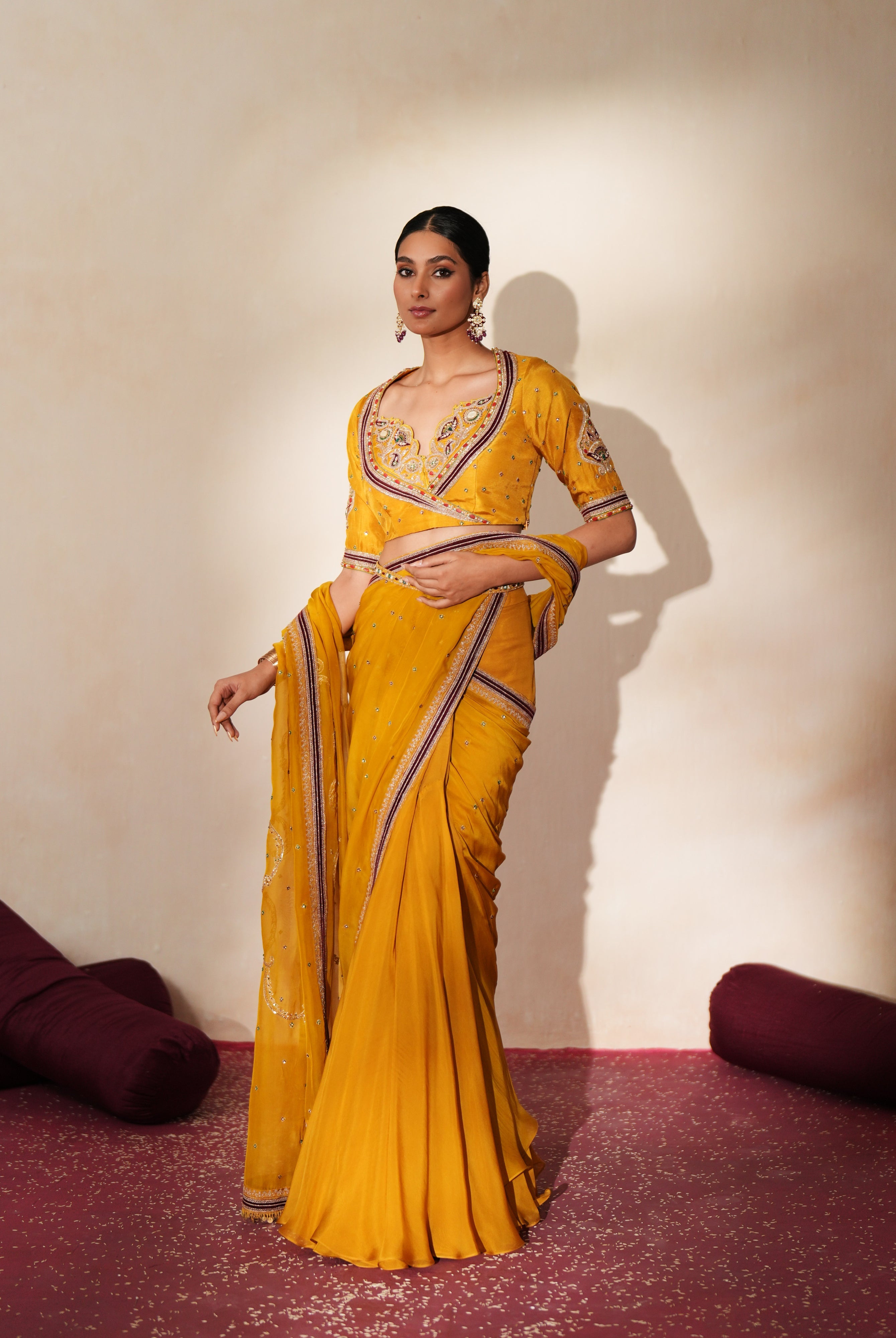 Woman in a golden yellow traditional outfit standing againsta beige wall on a red carpet.