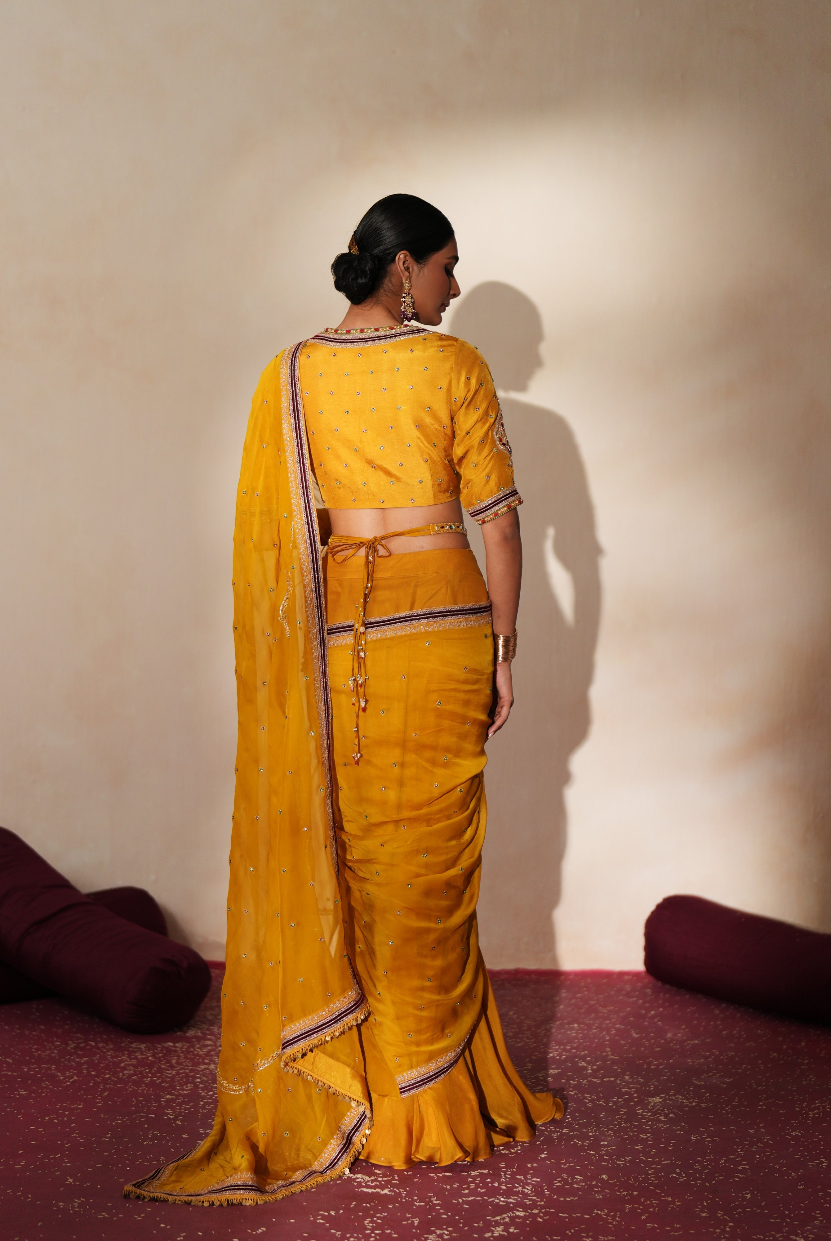 Woman in a golden yellow traditional outfit standing againsta beige wall on a red carpet.