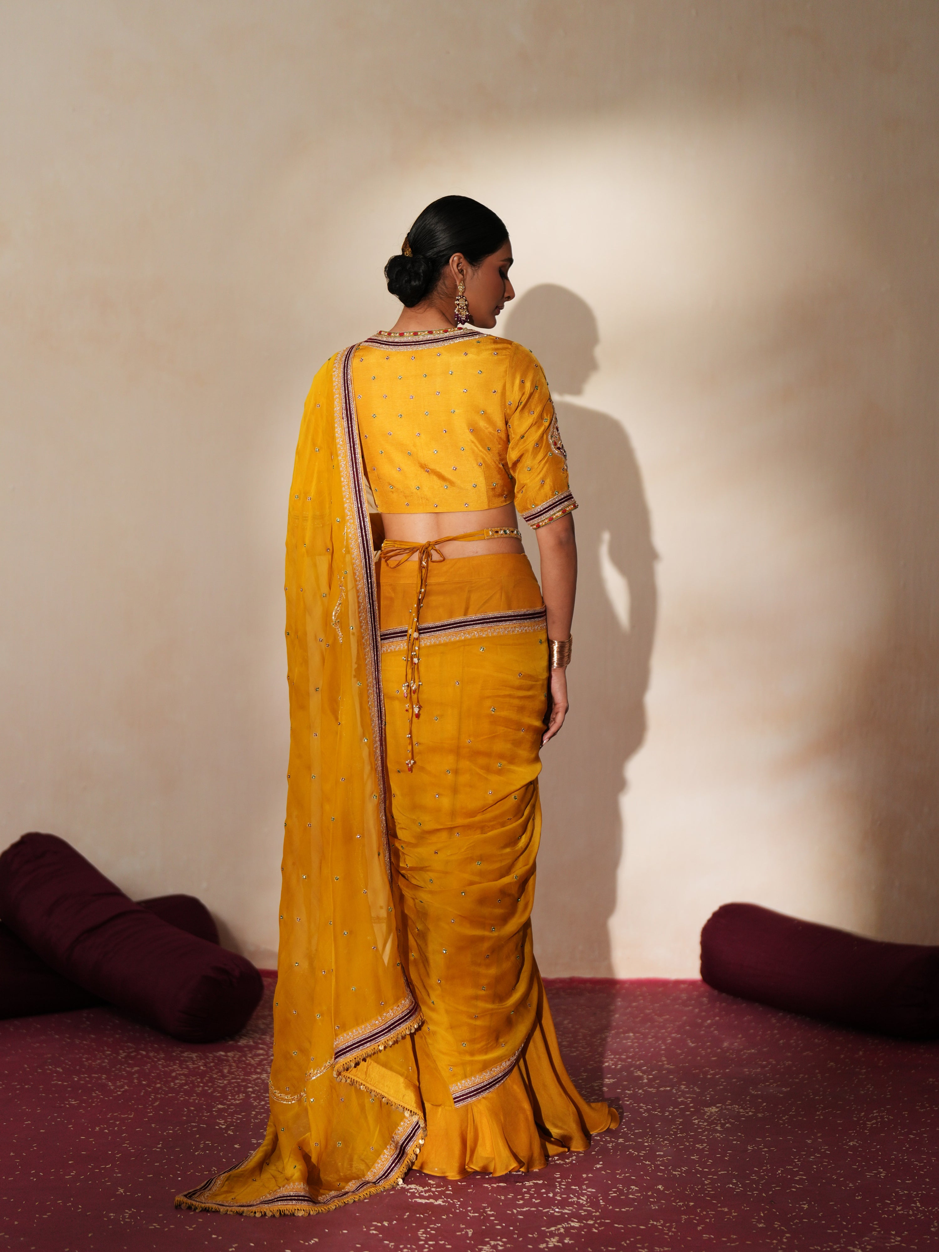 Woman in a golden yellow traditional outfit standing againsta beige wall on a red carpet.