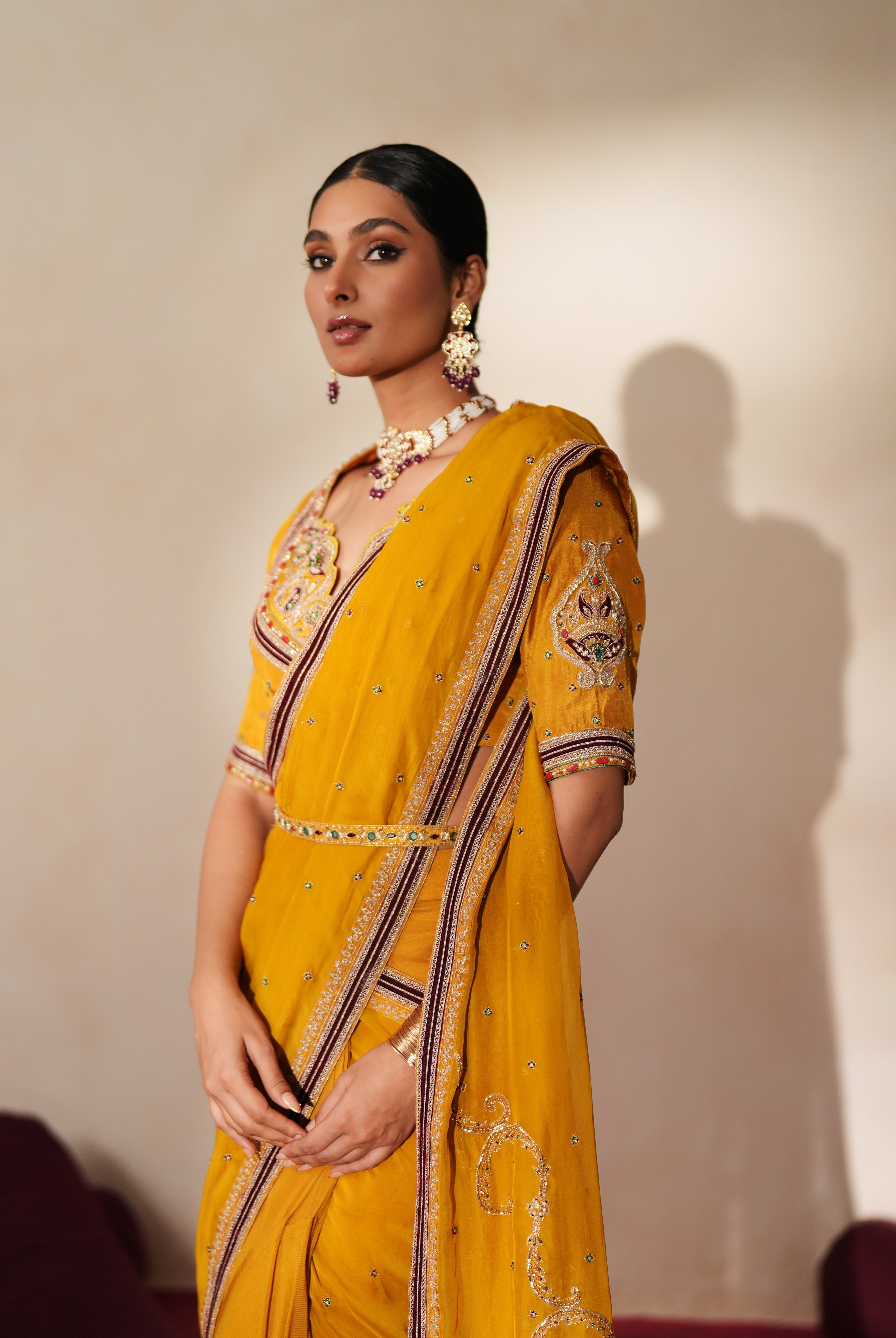 Woman in a golden yellow traditional outfit standing againsta beige wall on a red carpet.