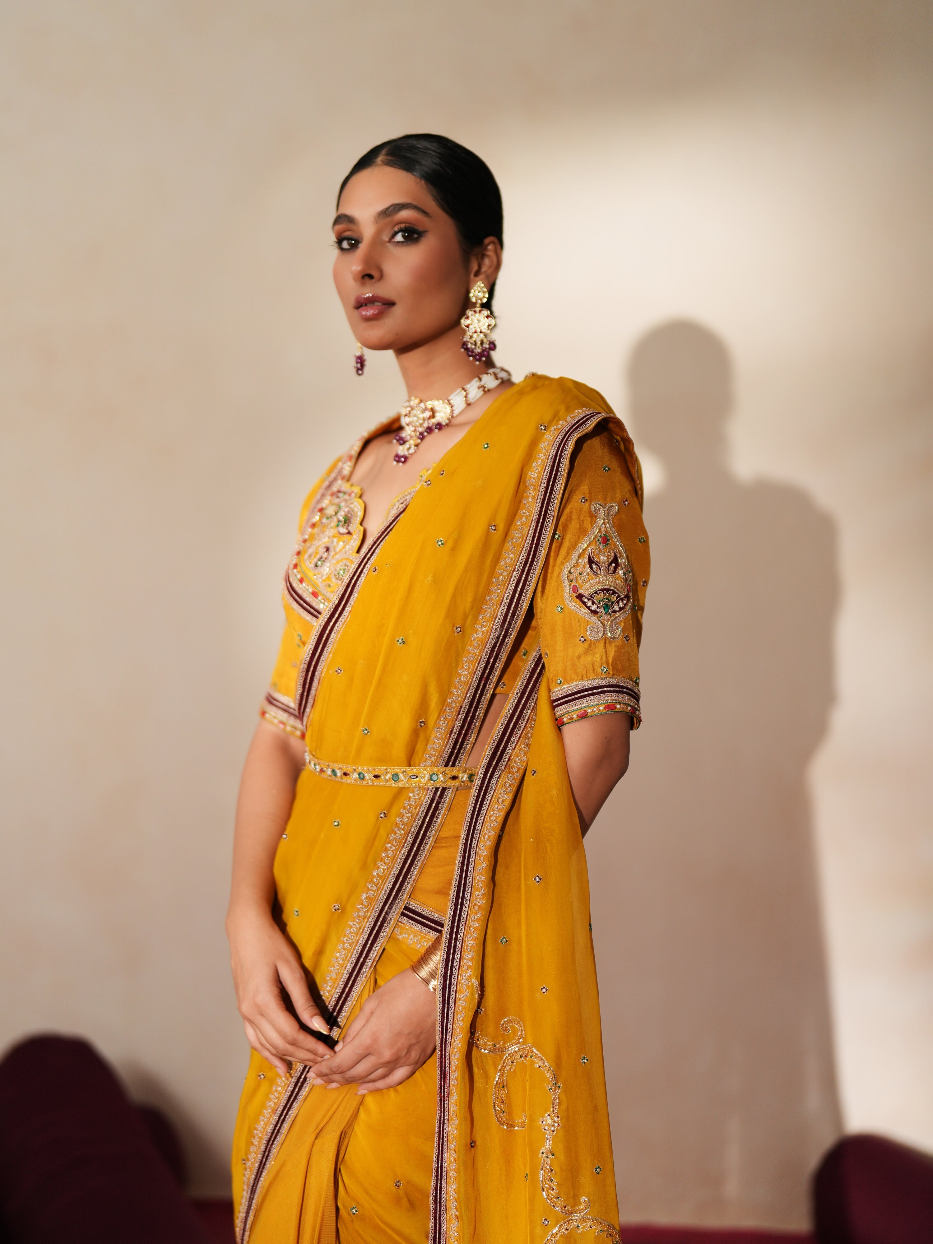 Woman in a golden yellow traditional outfit standing againsta beige wall on a red carpet.