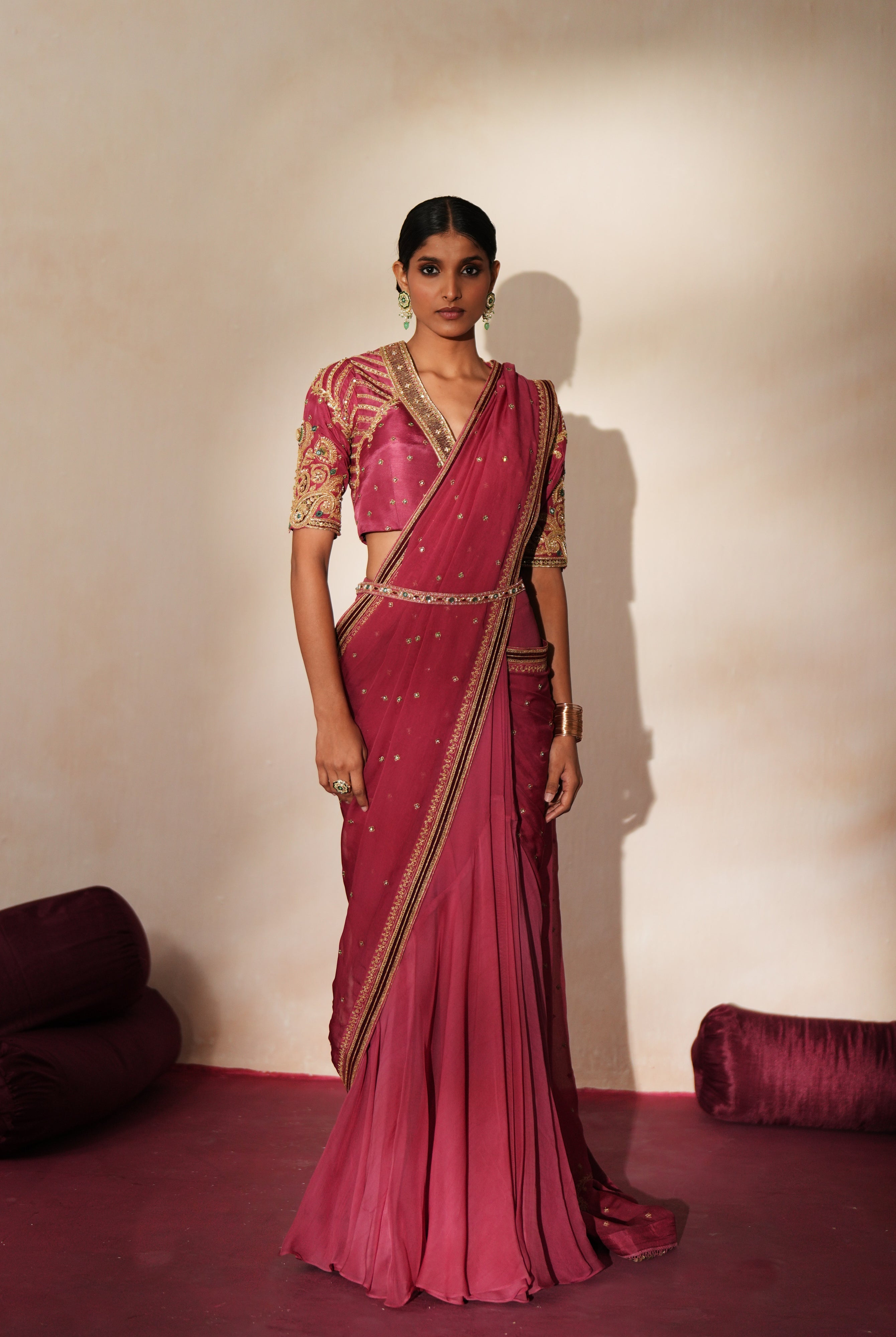 Woman in a mauve pink traditional outfit standing againsta beige wall on a red carpet.