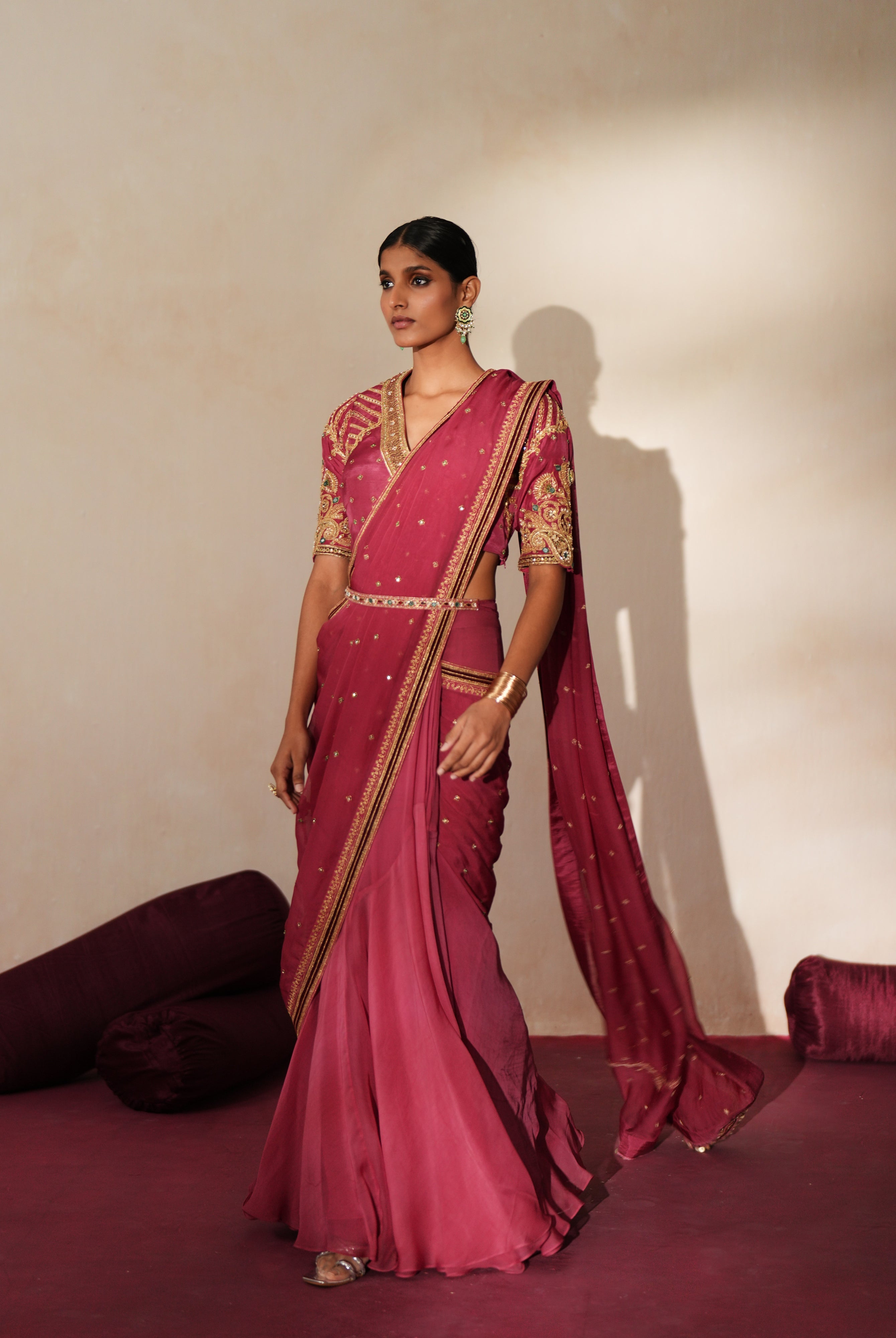 Woman in a mauve pink traditional outfit standing againsta beige wall on a red carpet.