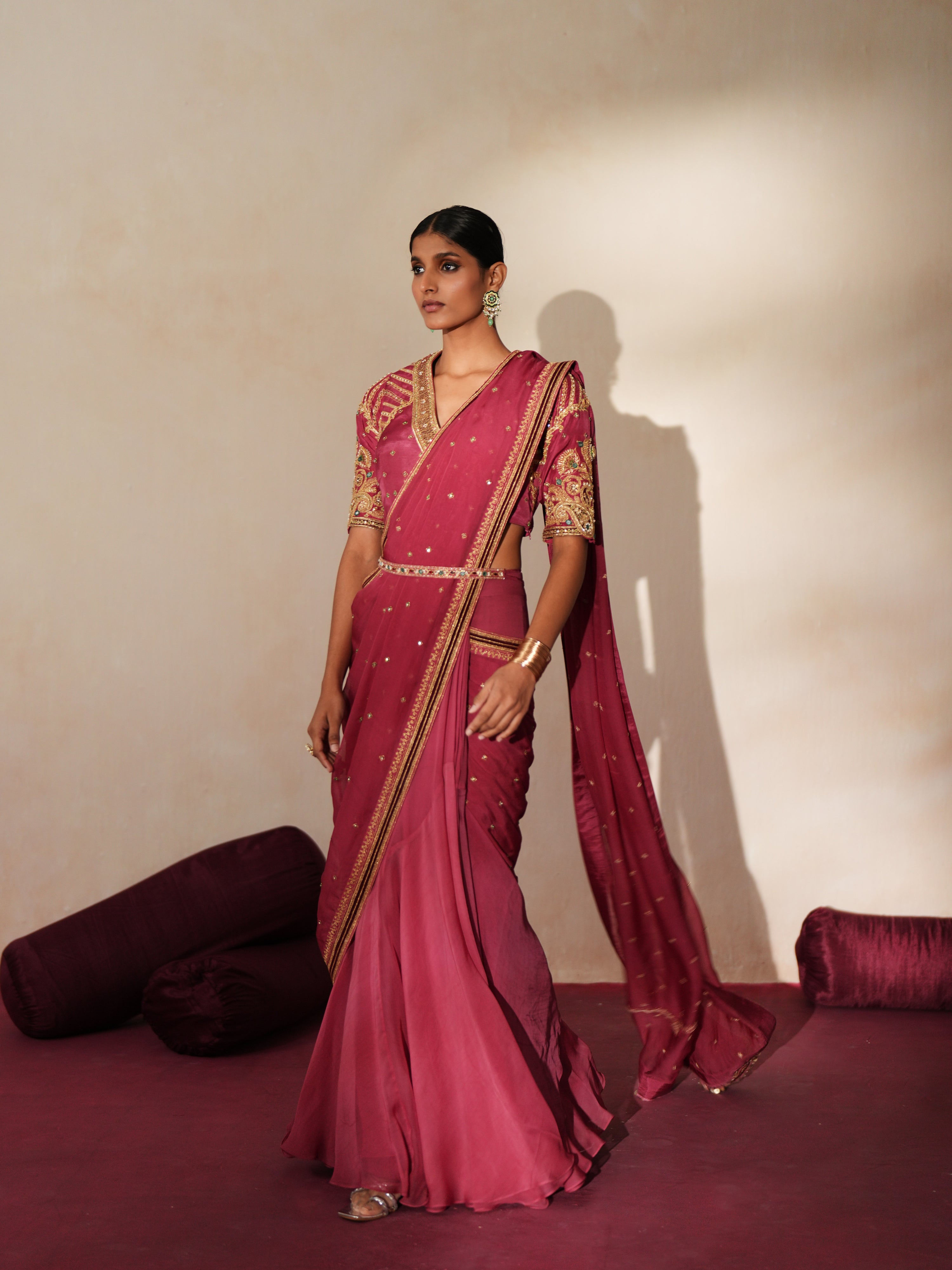 Woman in a mauve pink traditional outfit standing againsta beige wall on a red carpet.