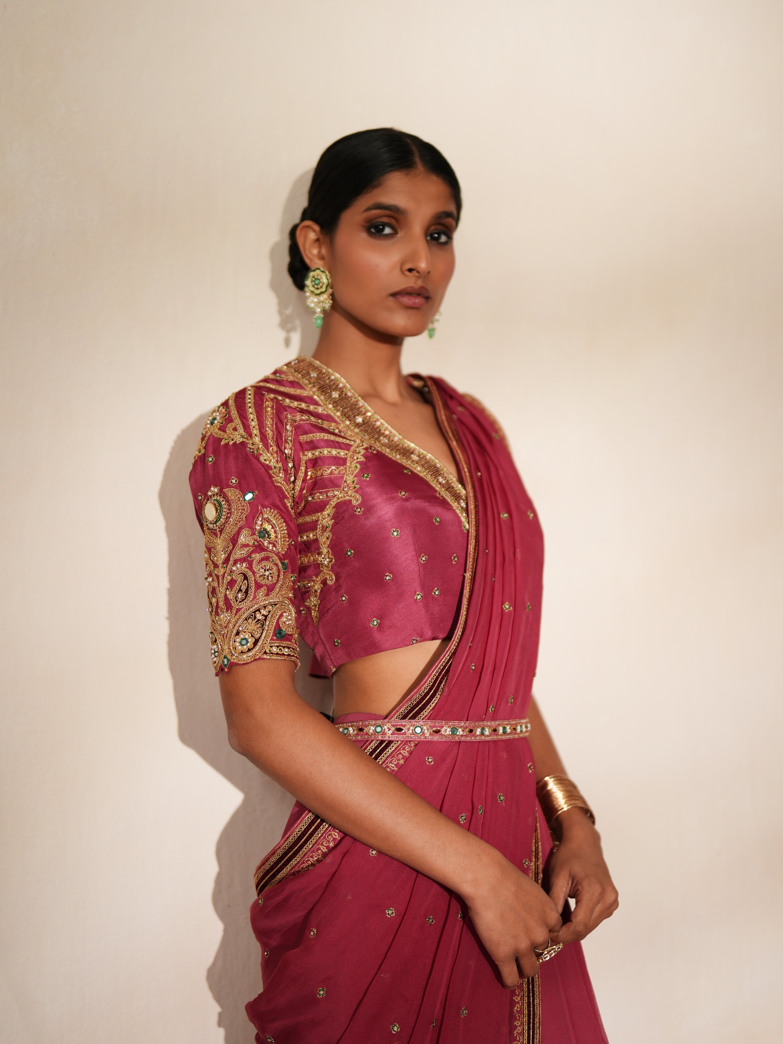 Woman in a mauve pink traditional outfit standing againsta beige wall on a red carpet.