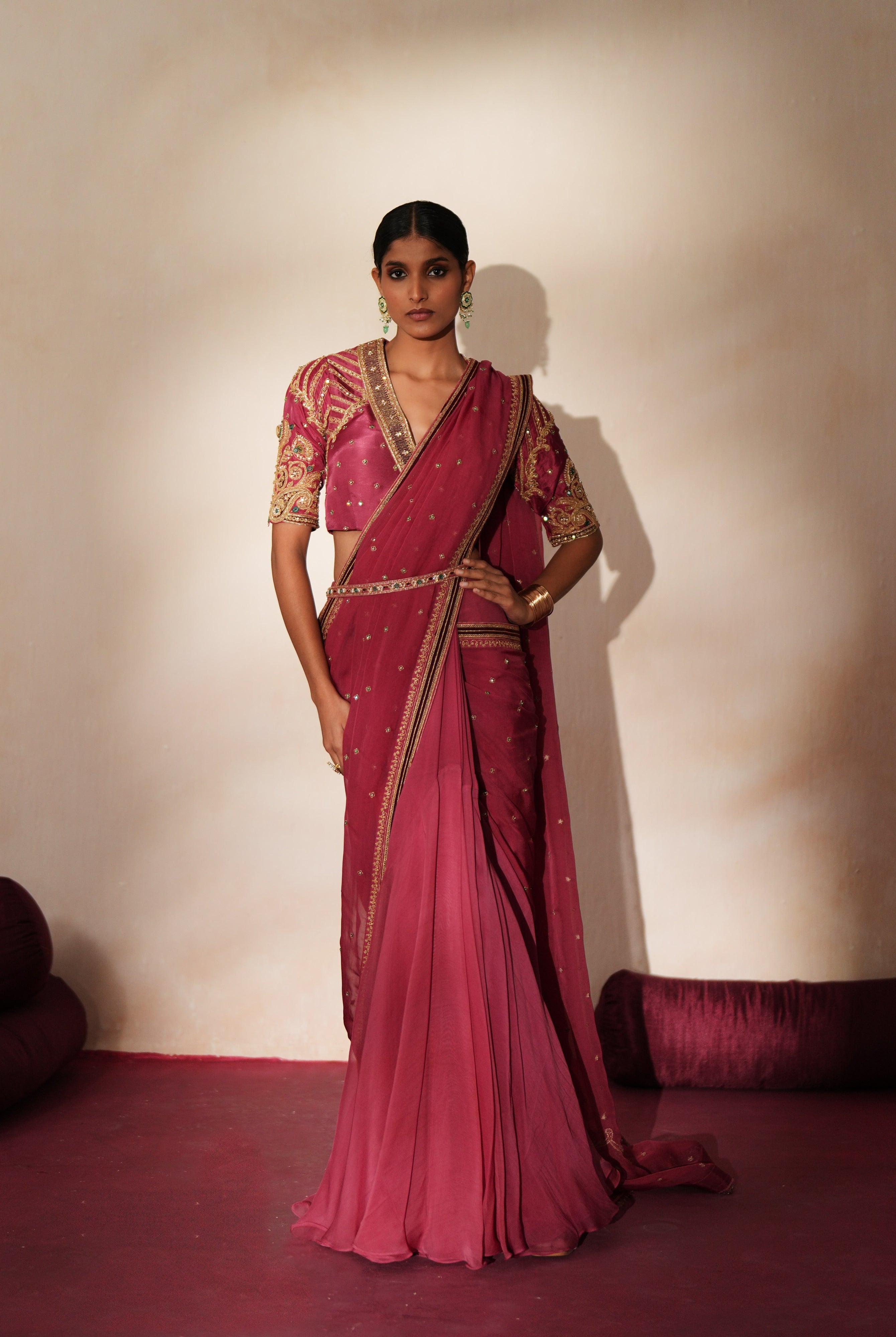 Woman in a mauve pink traditional outfit standing againsta beige wall on a red carpet.