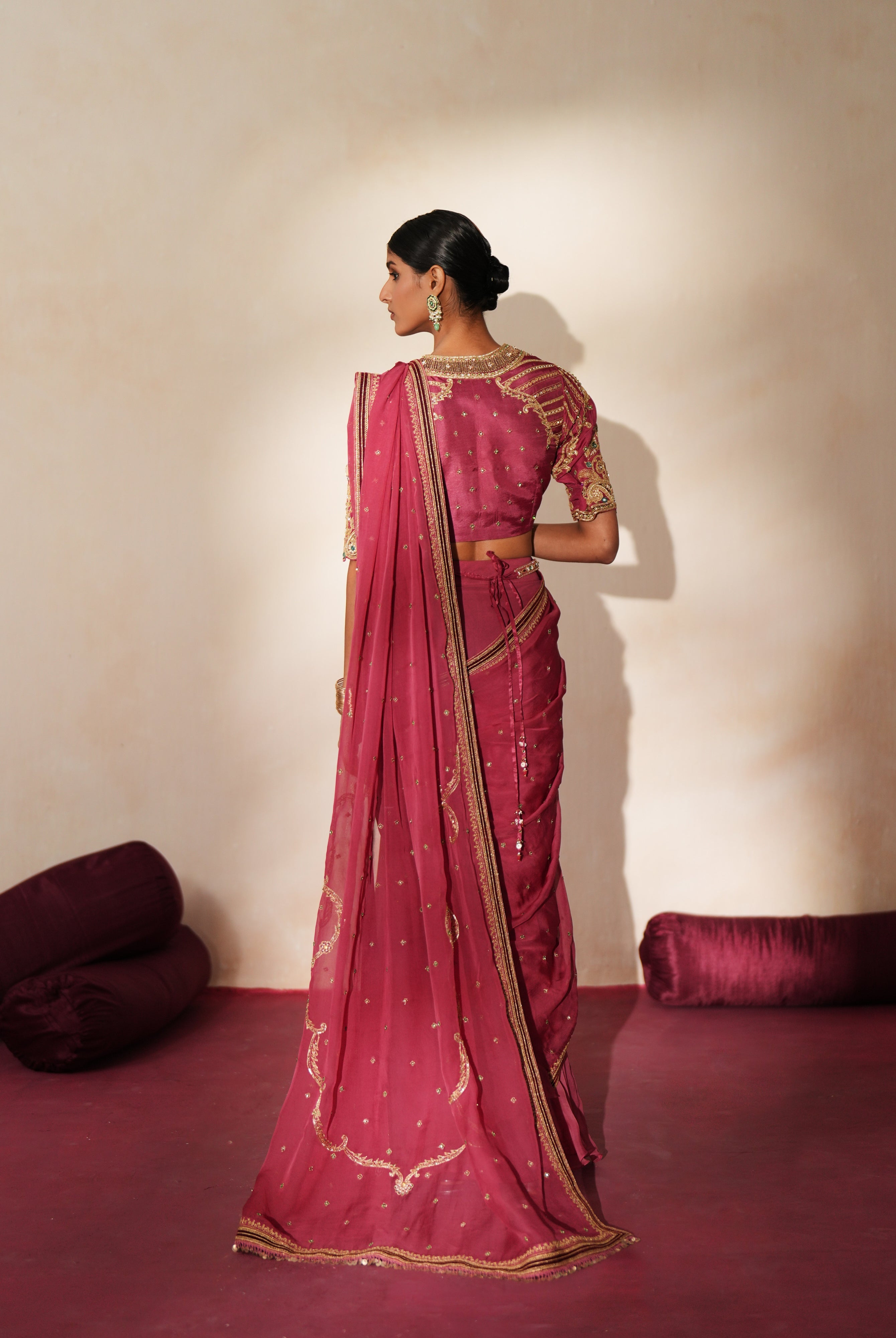Woman in a mauve pink traditional outfit standing againsta beige wall on a red carpet.