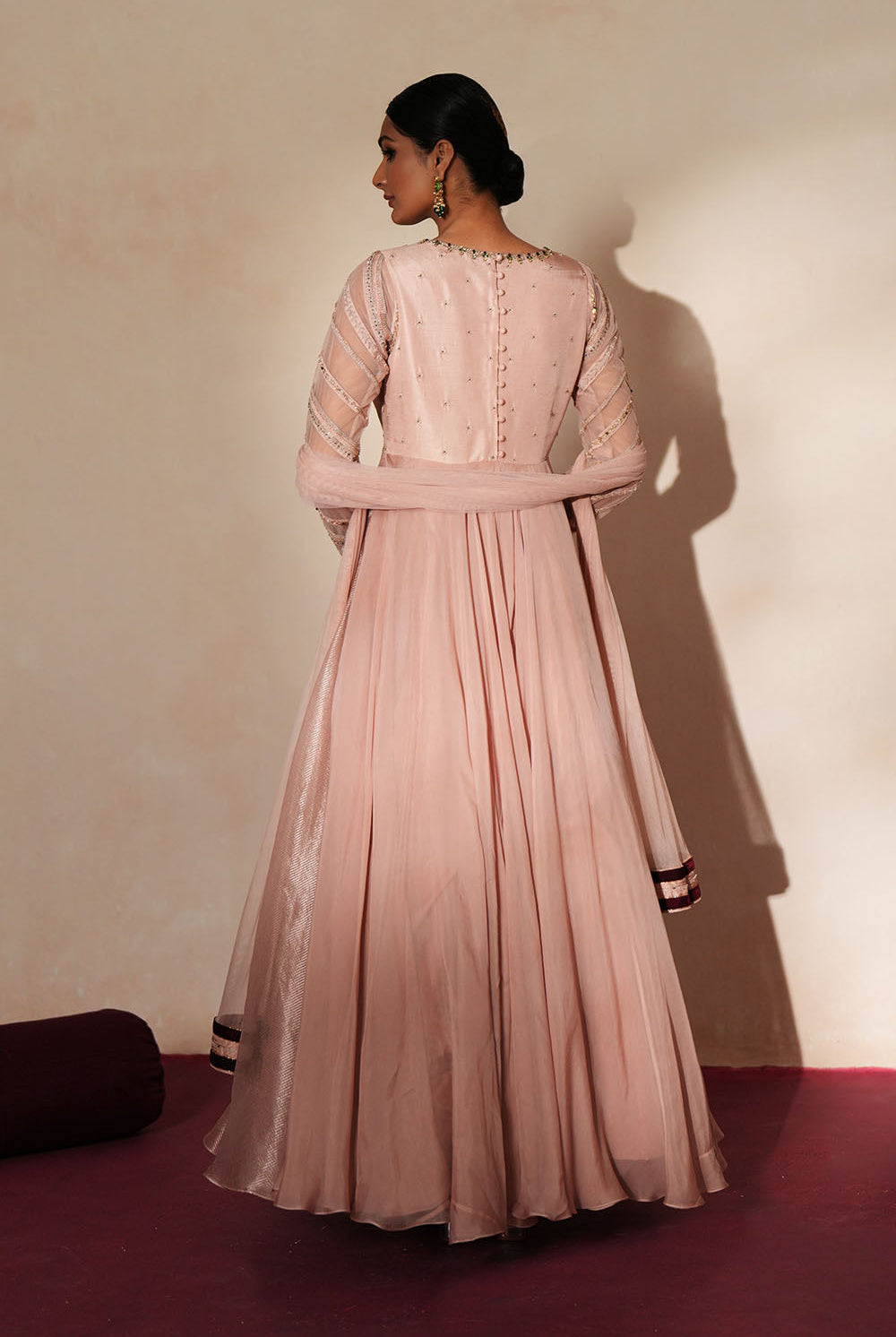 Woman in a soft pink traditional outfit standing againsta beige wall on a red carpet.