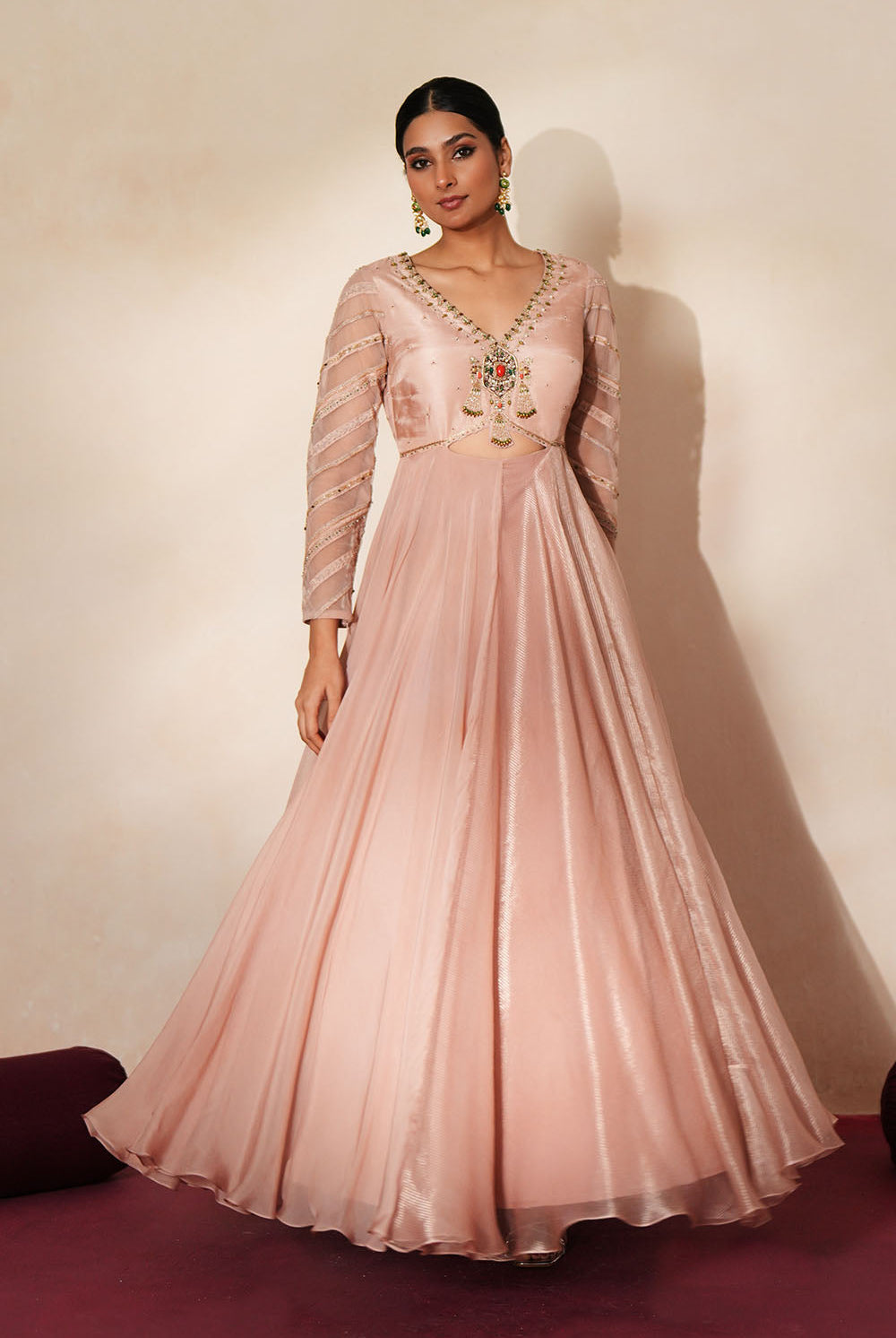 Woman in a soft pink traditional outfit standing againsta beige wall on a red carpet.