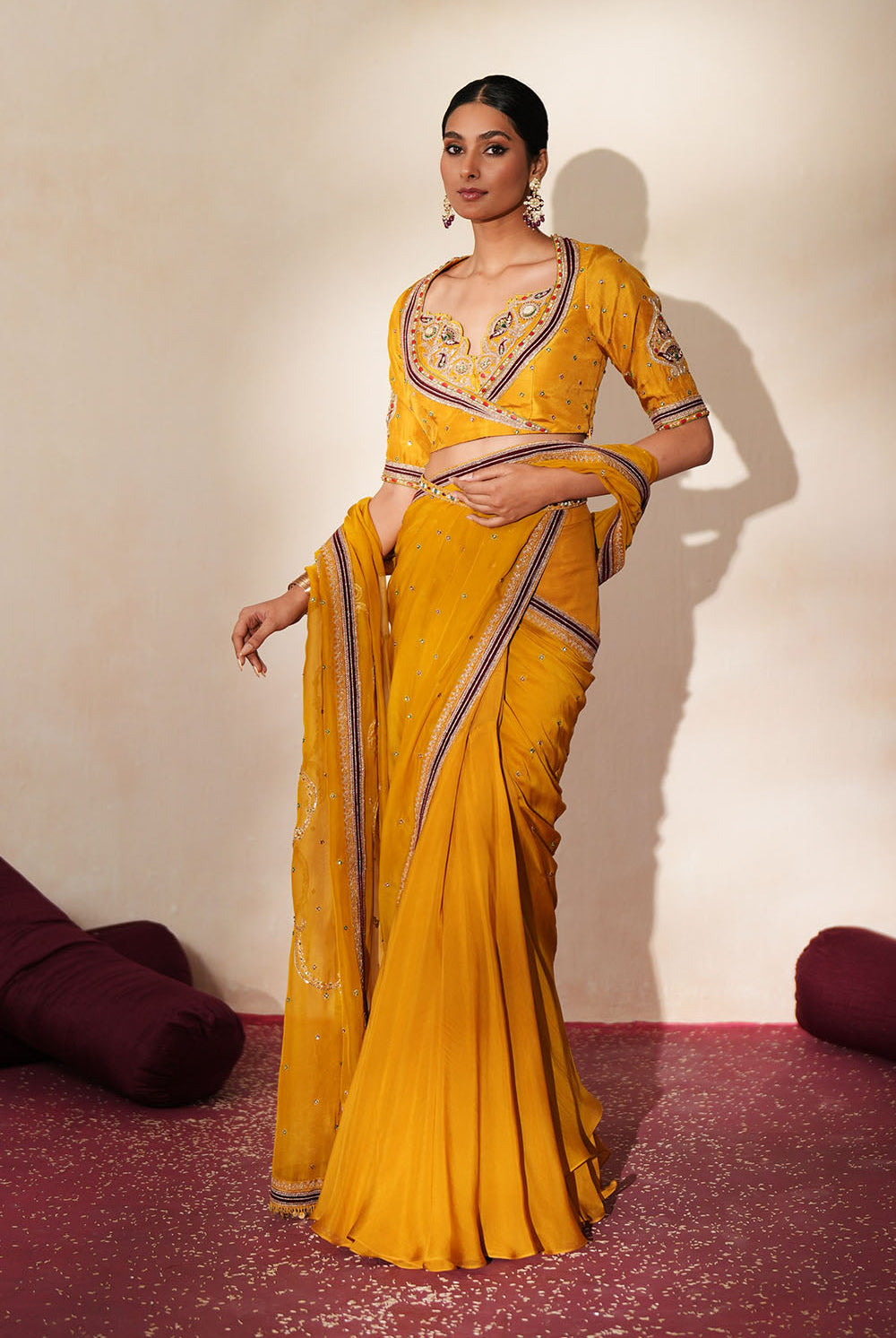 Woman in a golden yellow traditional outfit standing againsta beige wall on a red carpet.