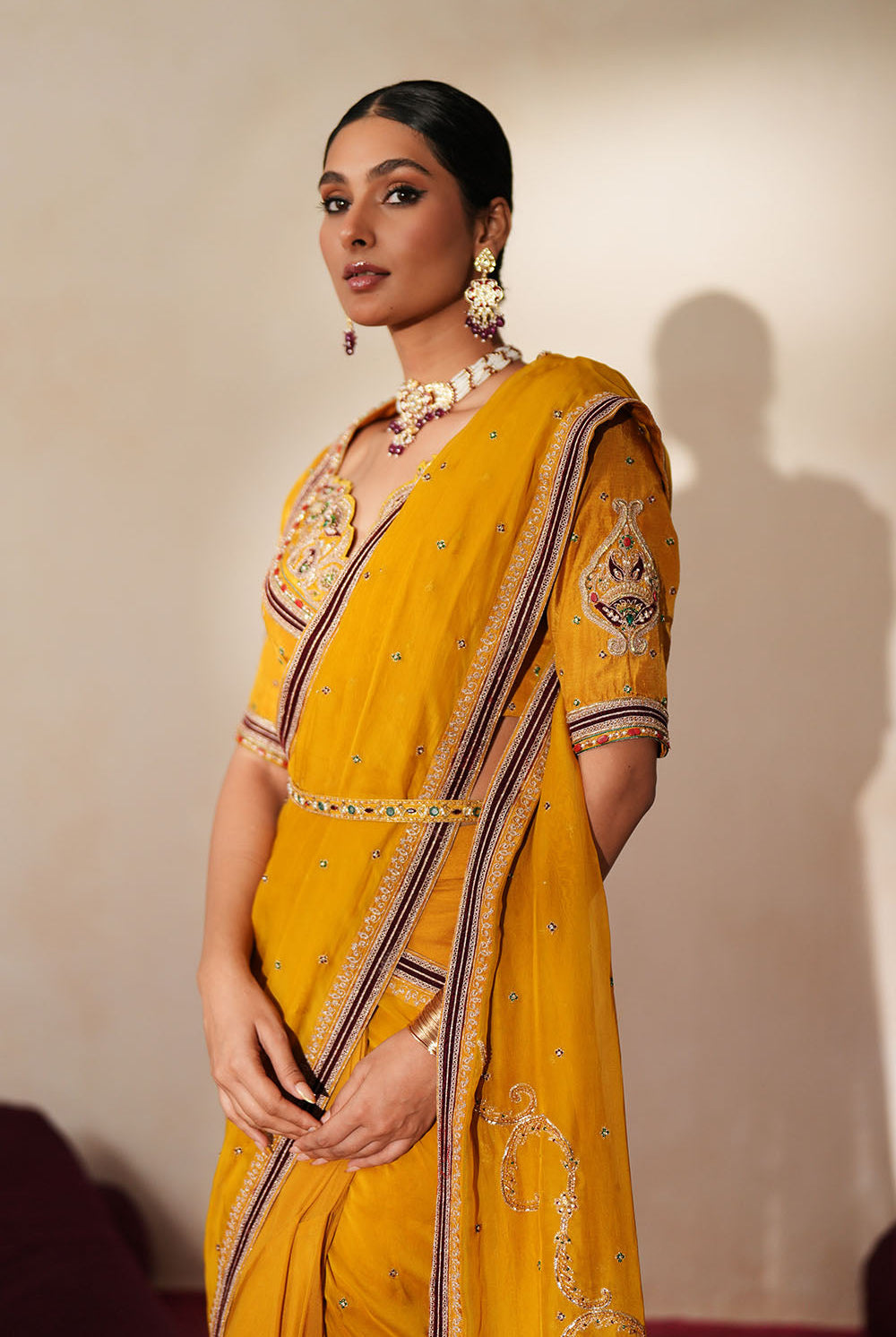 Woman in a golden yellow traditional outfit standing againsta beige wall on a red carpet.