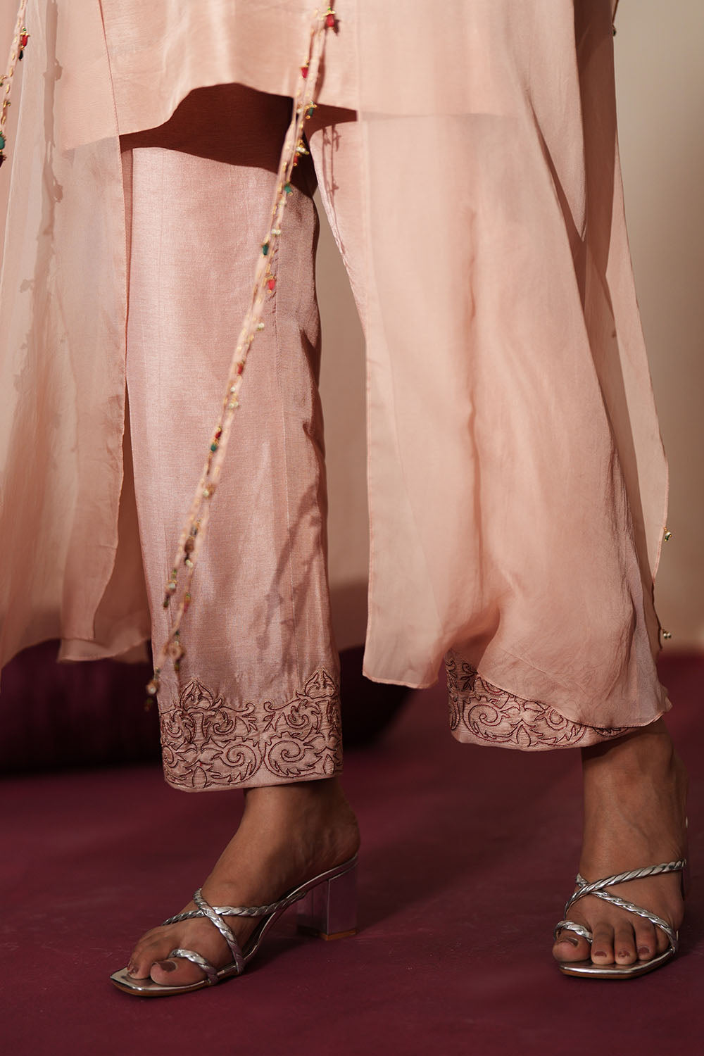 Woman in a soft pink traditional outfit standing againsta beige wall on a red carpet.