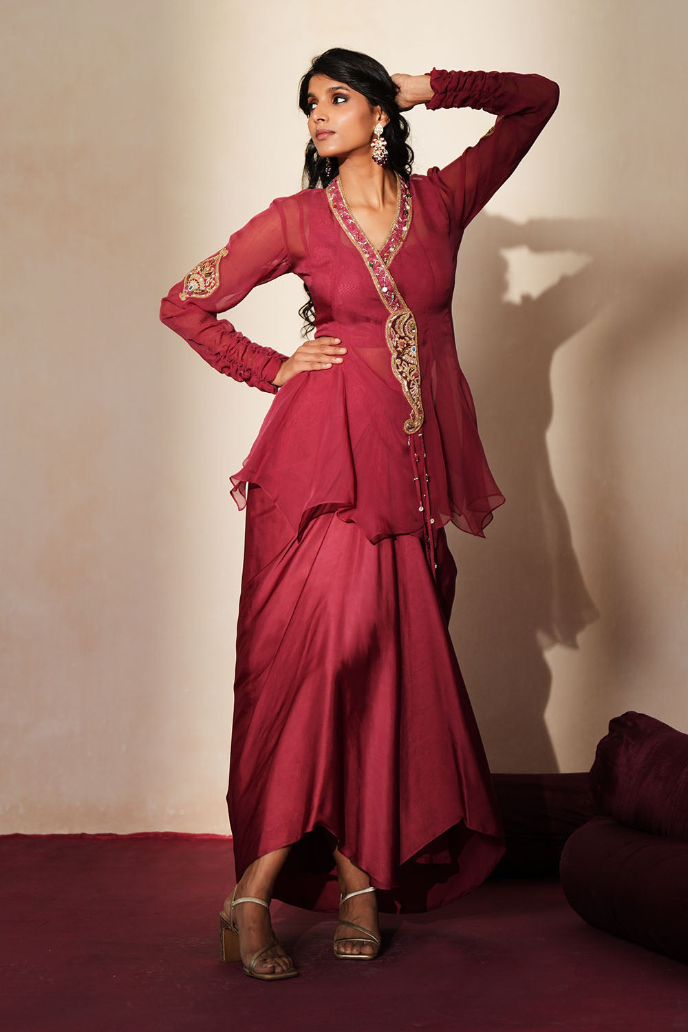 Woman in a mauve pink traditional outfit standing againsta beige wall on a red carpet.