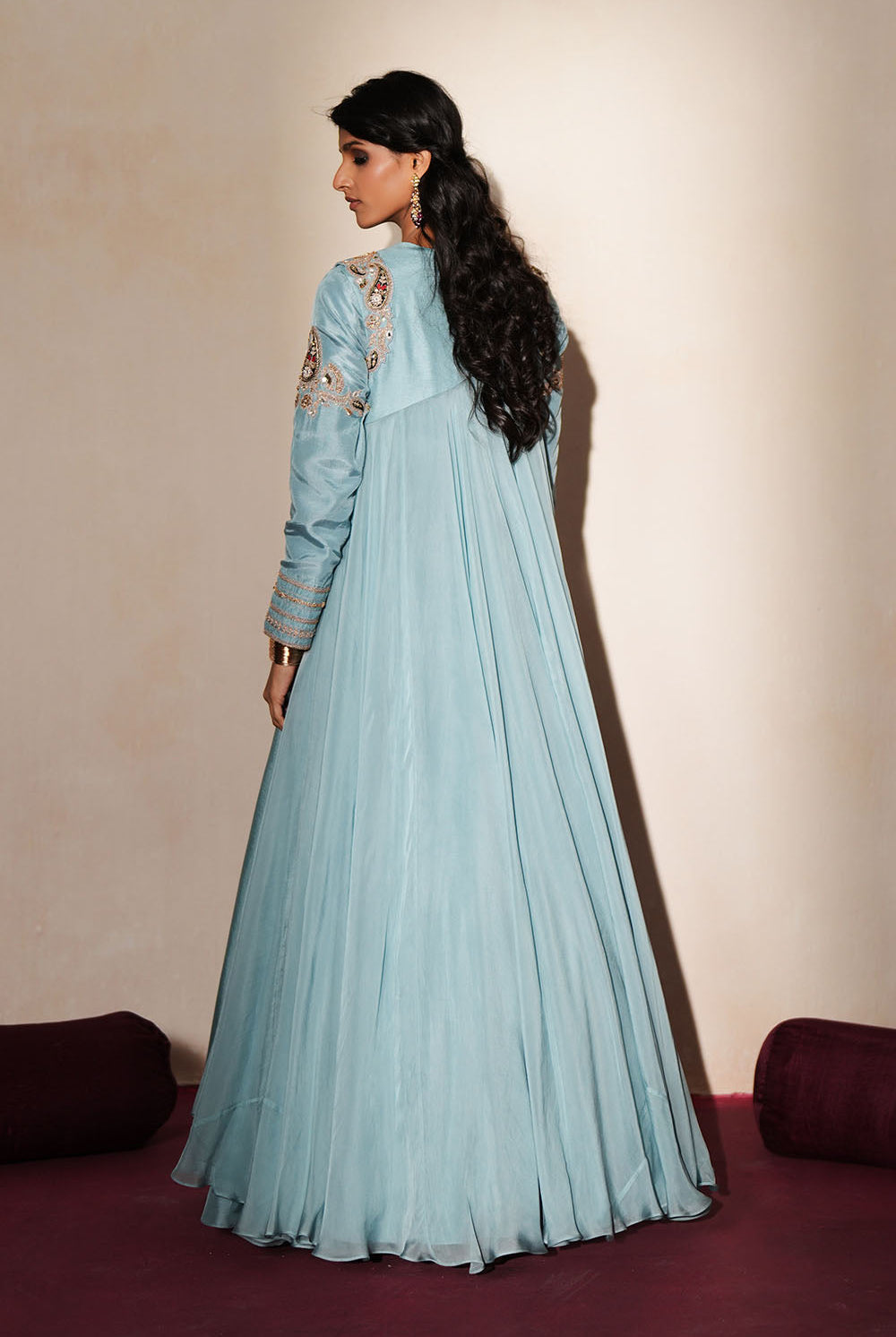 Woman in a pastel blue traditional outfit standing againsta beige wall on a red carpet.