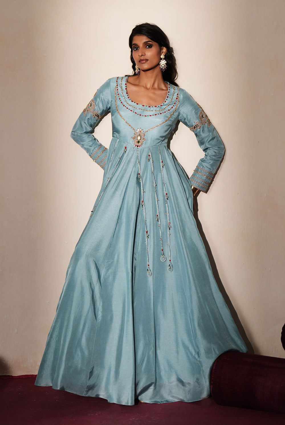 Woman in a pastel blue traditional outfit standing againsta beige wall on a red carpet.