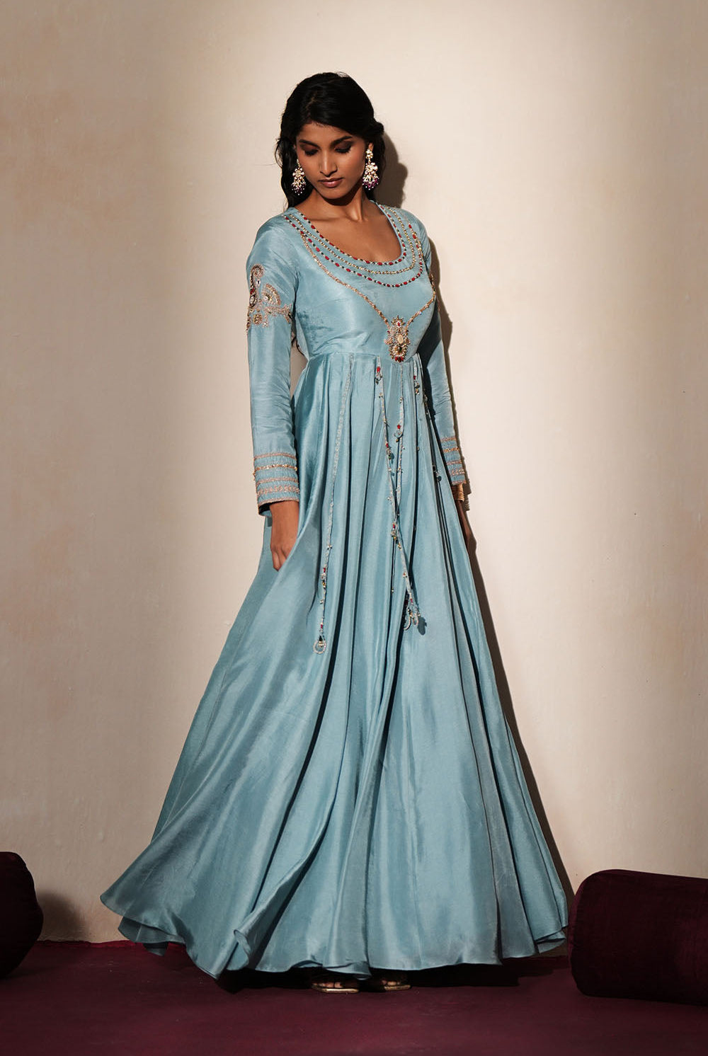 Woman in a pastel blue traditional outfit standing againsta beige wall on a red carpet.