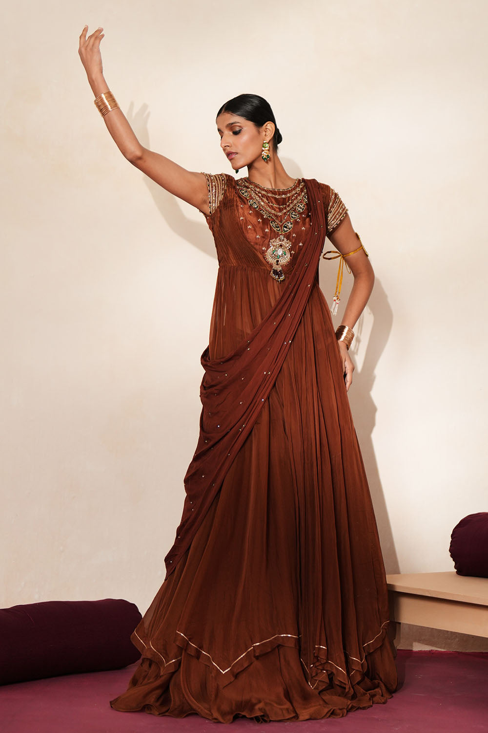 Woman in a mettalic brown traditional outfit standing againsta beige wall on a red carpet.