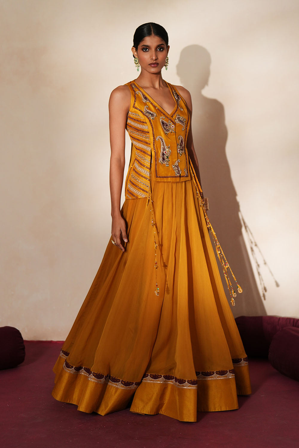 Woman in a golden yellow traditional outfit standing againsta beige wall on a red carpet.