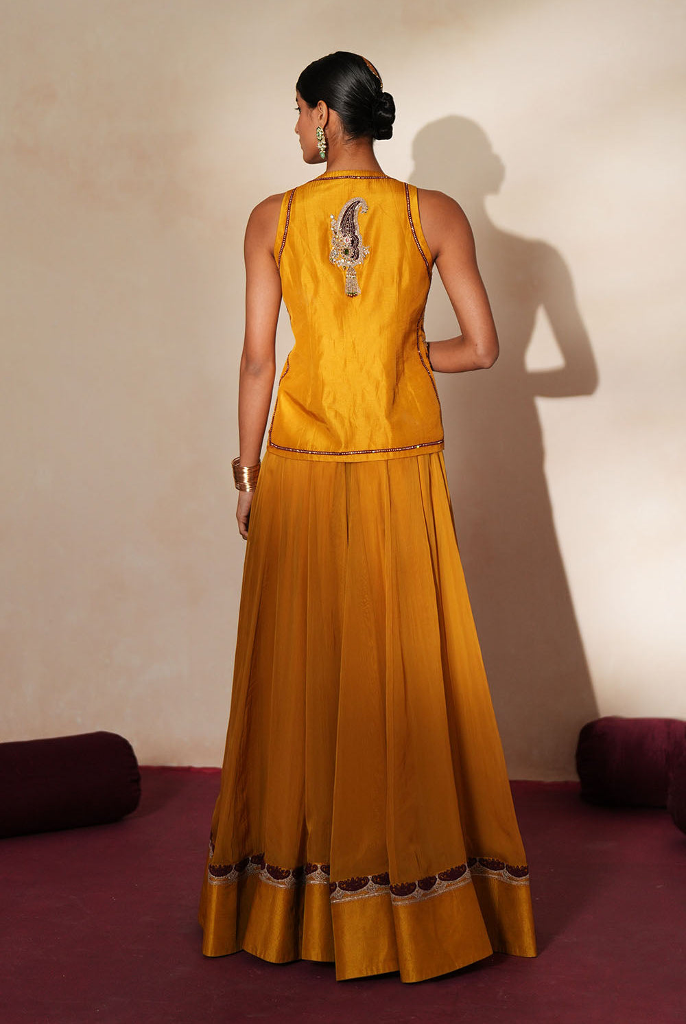 Woman in a golden yellow traditional outfit standing againsta beige wall on a red carpet.
