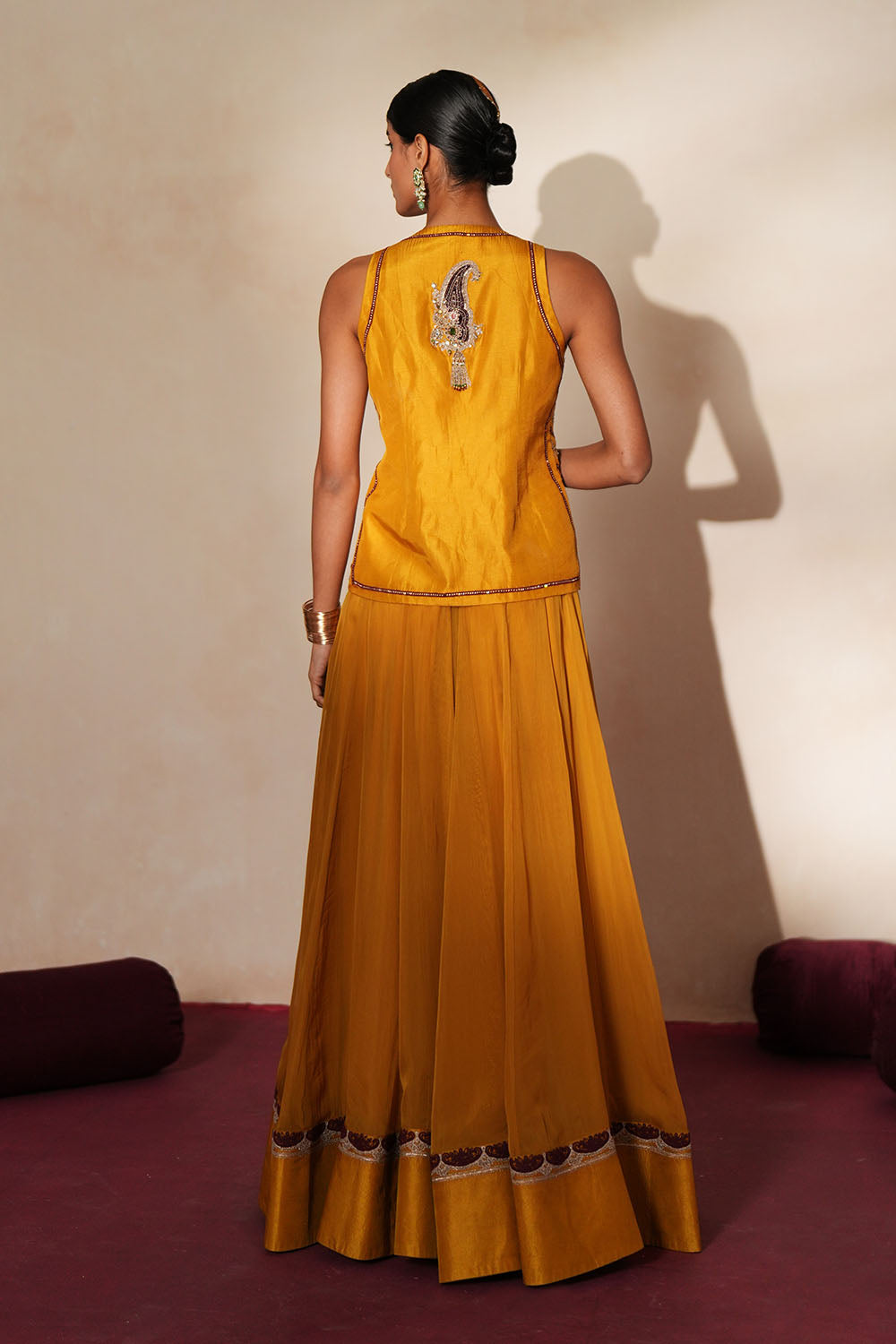 Woman in a golden yellow traditional outfit standing againsta beige wall on a red carpet.