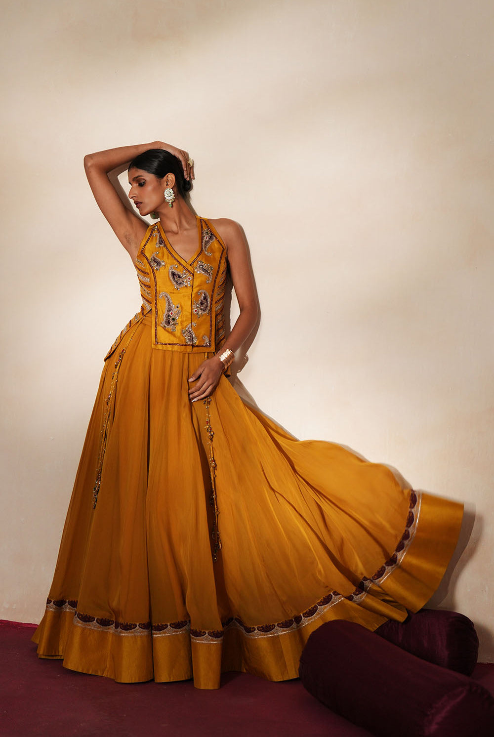 Woman in a golden yellow traditional outfit standing againsta beige wall on a red carpet.