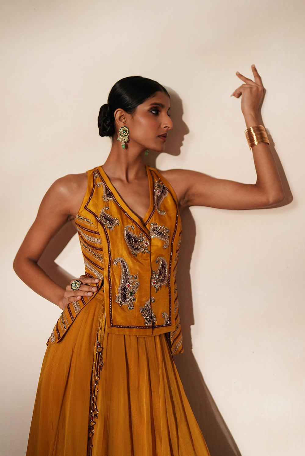Woman in a golden yellow traditional outfit standing againsta beige wall on a red carpet.