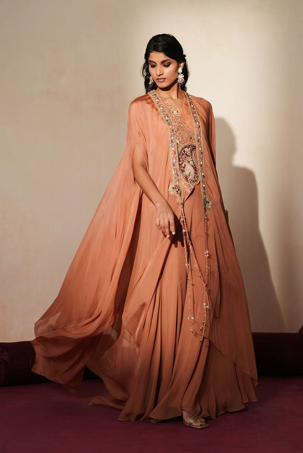 Woman in a metallic mocha traditional outfit standing againsta beige wall on a red carpet.