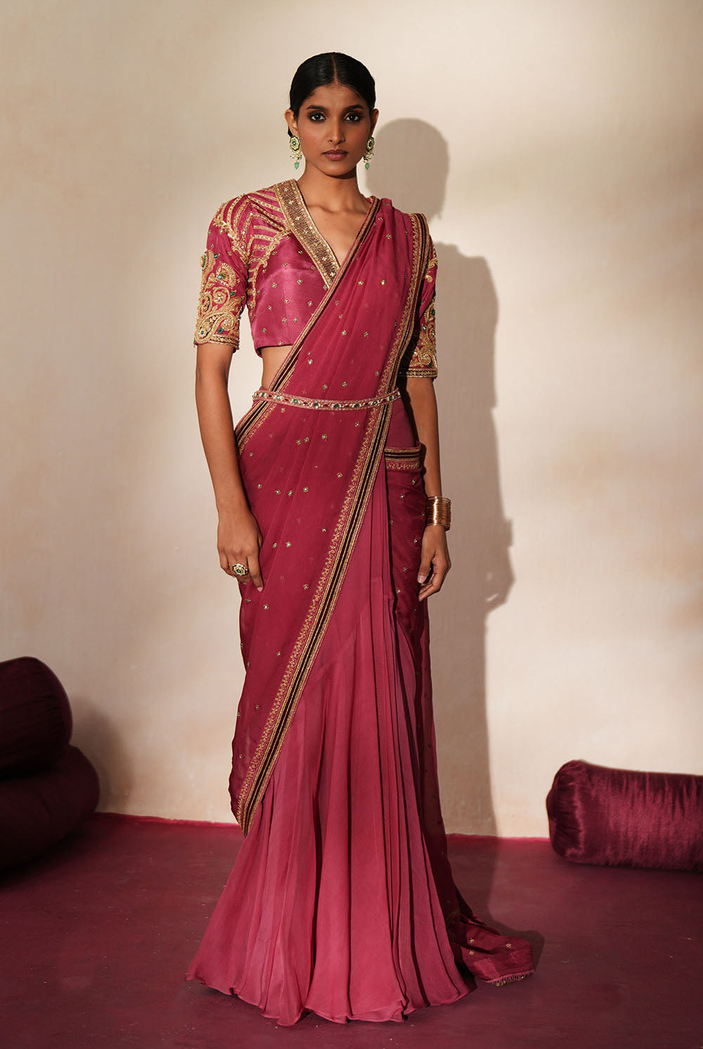 Woman in a mauve pink traditional outfit standing againsta beige wall on a red carpet.