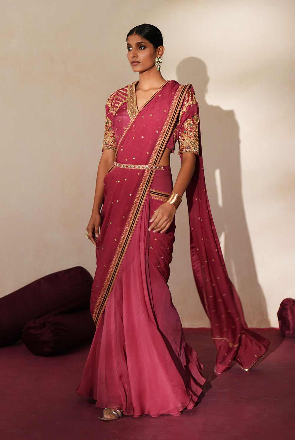 Woman in a mauve pink traditional outfit standing againsta beige wall on a red carpet.