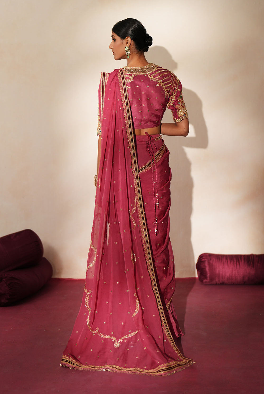 Woman in a mauve pink traditional outfit standing againsta beige wall on a red carpet.