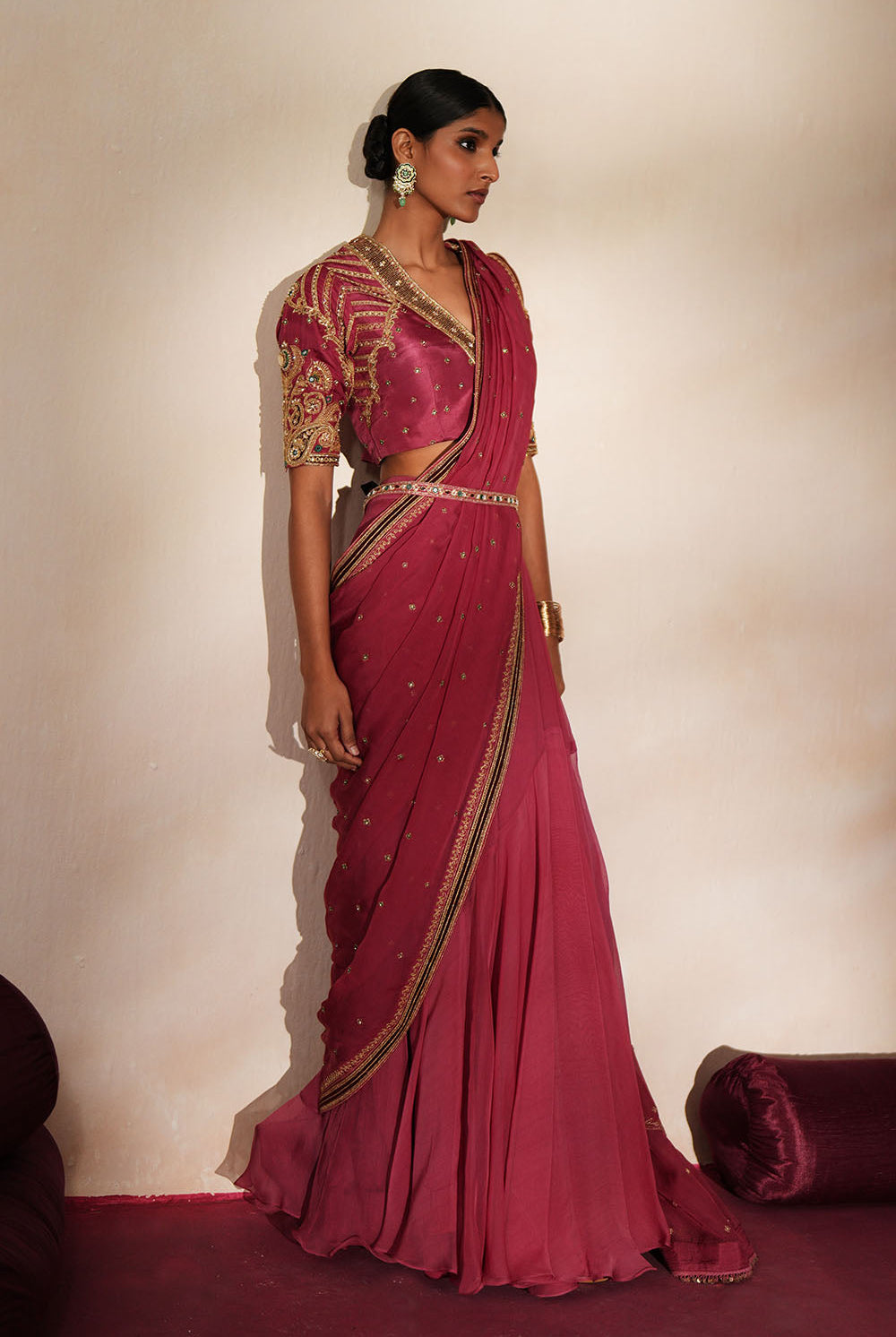 Woman in a mauve pink traditional outfit standing againsta beige wall on a red carpet.