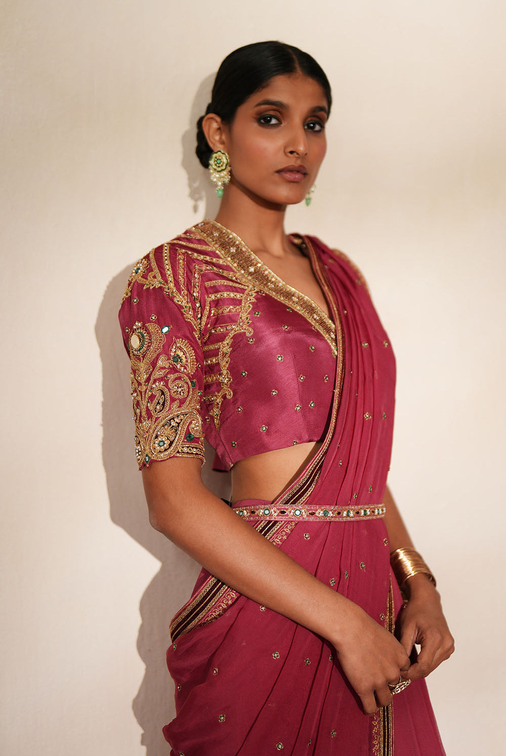 Woman in a mauve pink traditional outfit standing againsta beige wall on a red carpet.