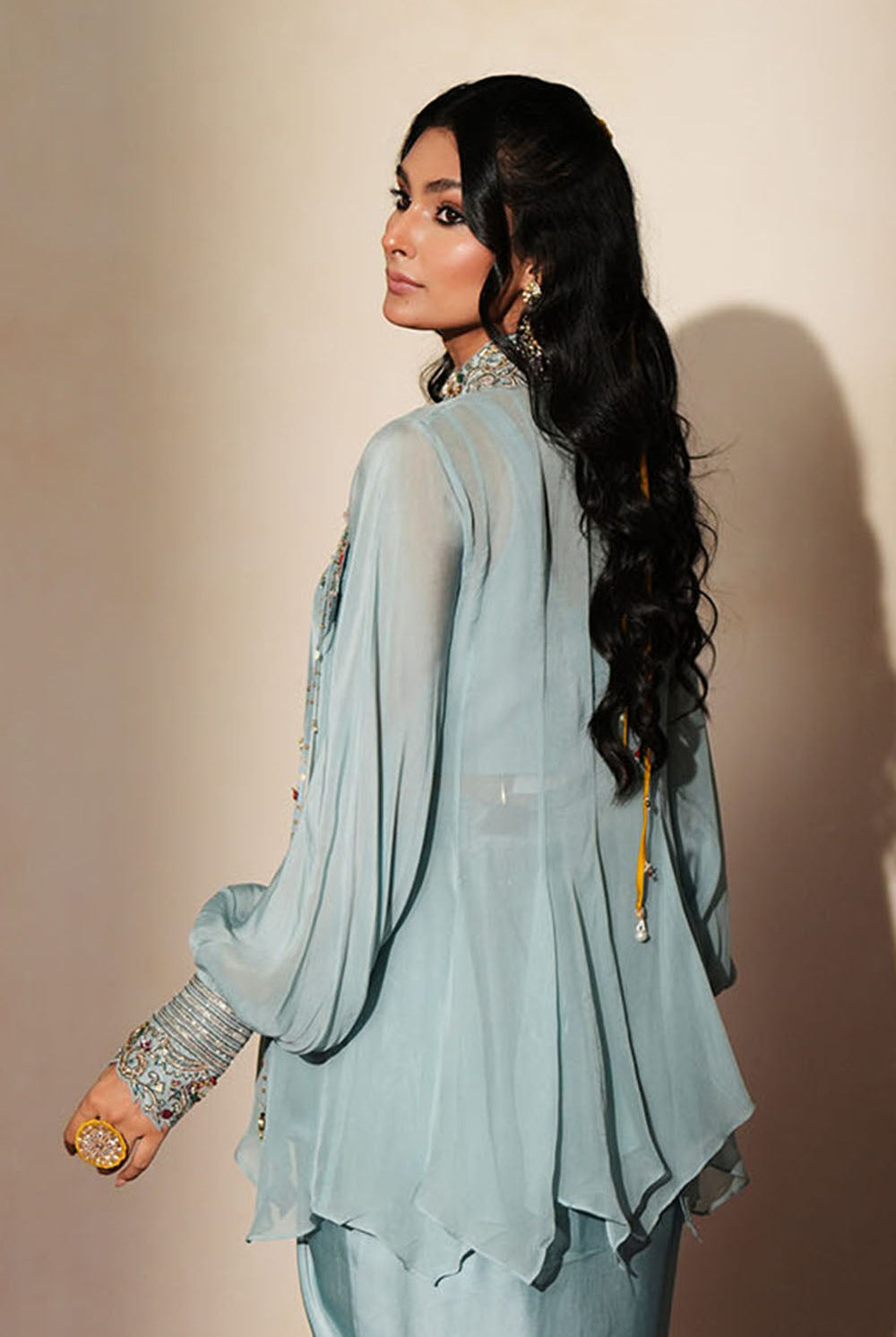 Woman in a pastel blue traditional outfit standing againsta beige wall on a red carpet.