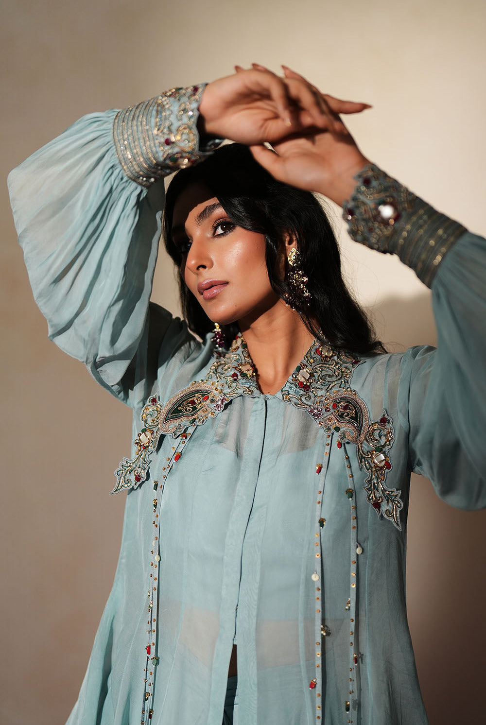 Woman in a pastel blue traditional outfit standing againsta beige wall on a red carpet.