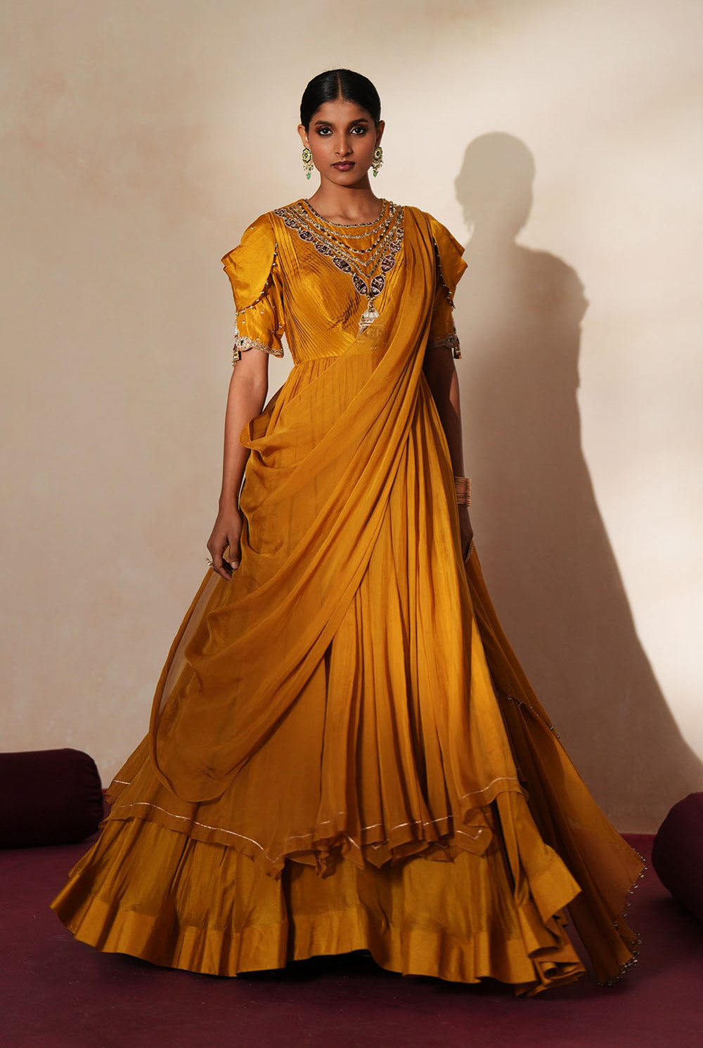 Woman in a golden yellow traditional outfit standing againsta beige wall on a red carpet.