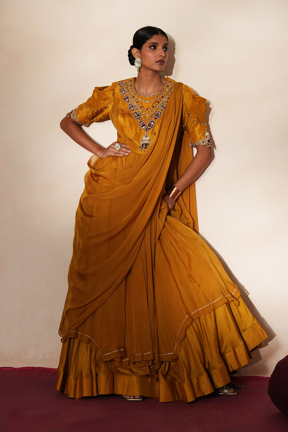 Woman in a golden yellow traditional outfit standing againsta beige wall on a red carpet.
