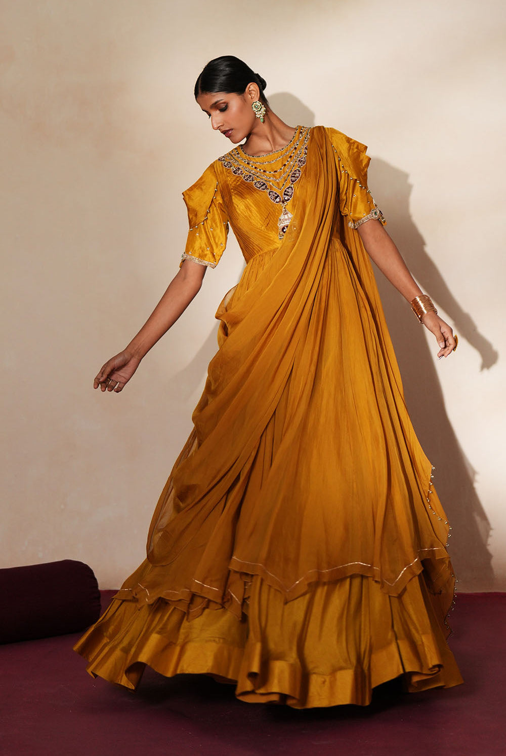 Woman in a golden yellow traditional outfit standing againsta beige wall on a red carpet.