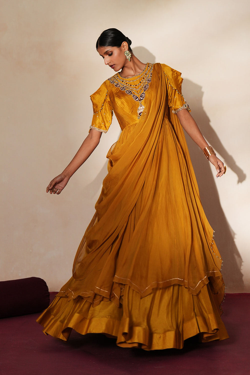 Woman in a golden yellow traditional outfit standing againsta beige wall on a red carpet.