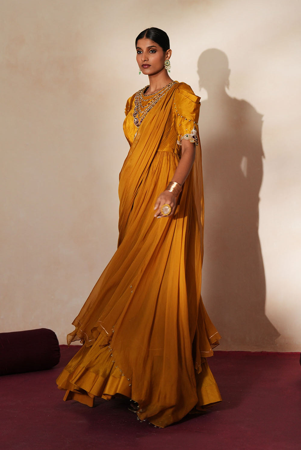 Woman in a golden yellow traditional outfit standing againsta beige wall on a red carpet.